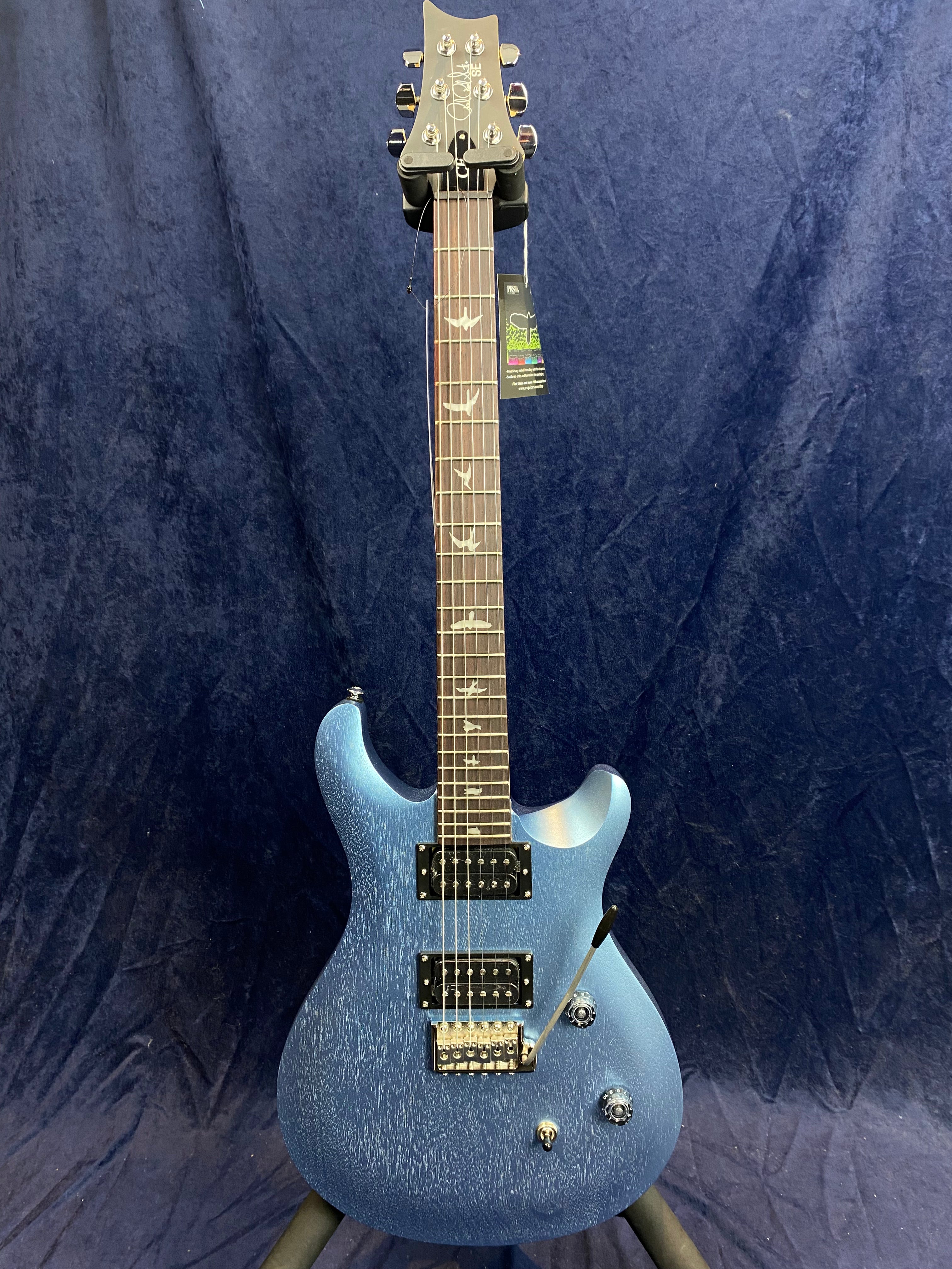 Blue electric guitar with two humbucker pickups, a tremolo bar, and bird inlays on the dark fretboard, displayed against a dark blue background.