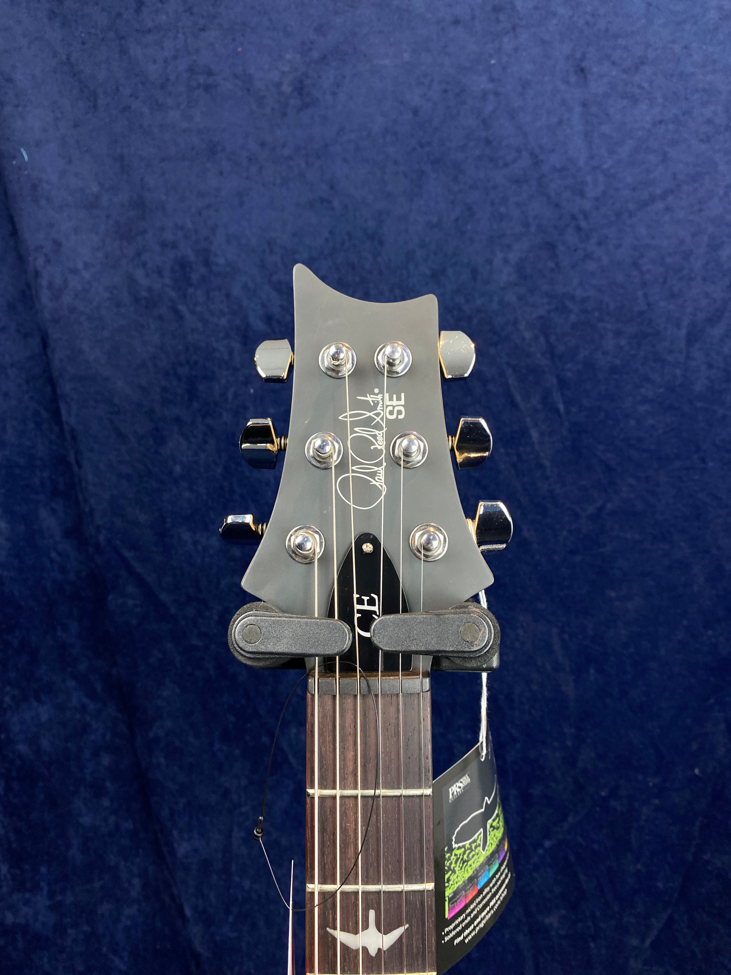 Close-up of a PRS SE electric guitar headstock with six tuning pegs, silver logo, and a bird inlay on the dark wood fretboard.