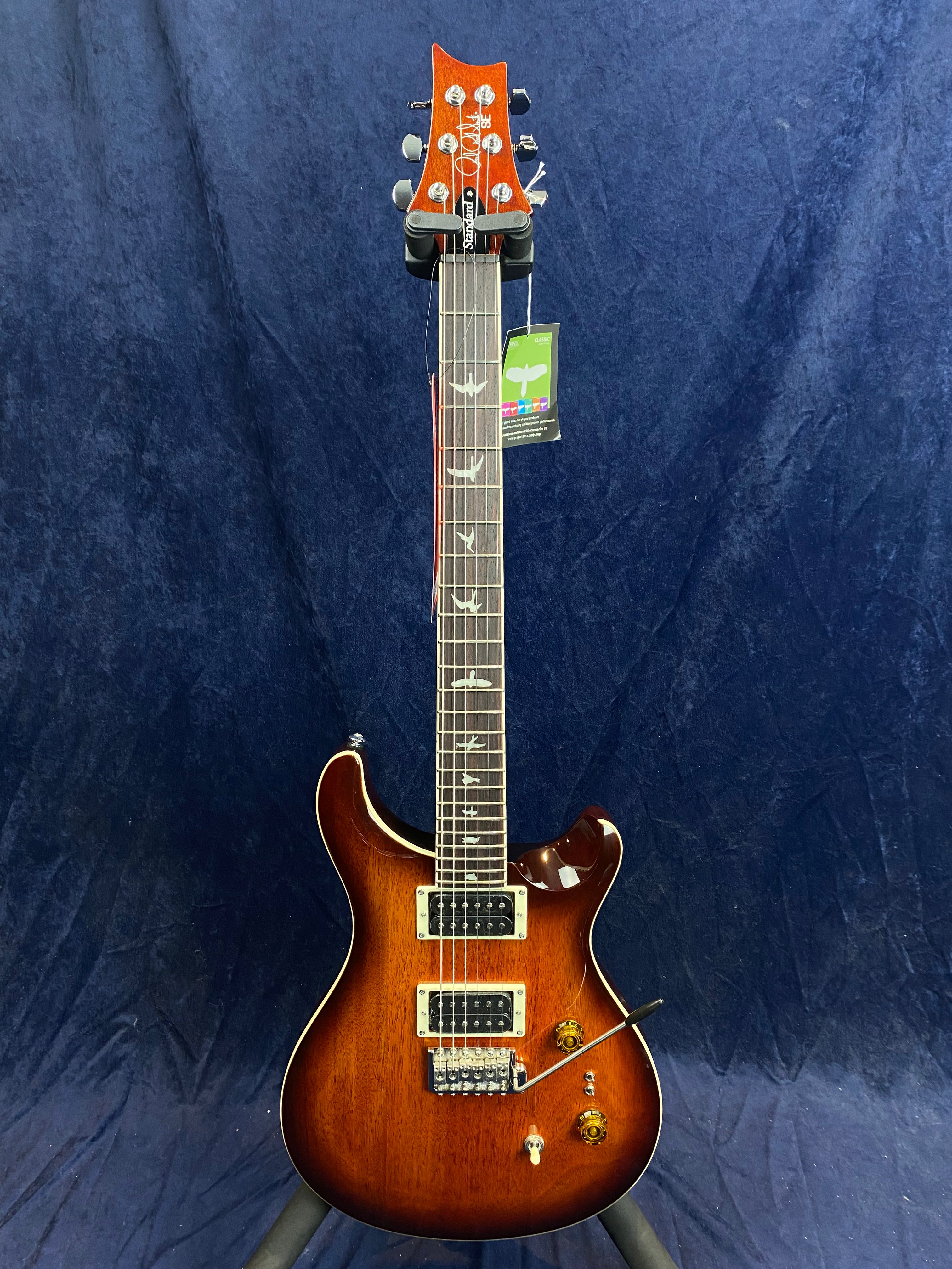 Sunburst electric guitar with bird inlays on the fretboard, two humbucker pickups, and gold control knobs, displayed upright against a dark blue background.