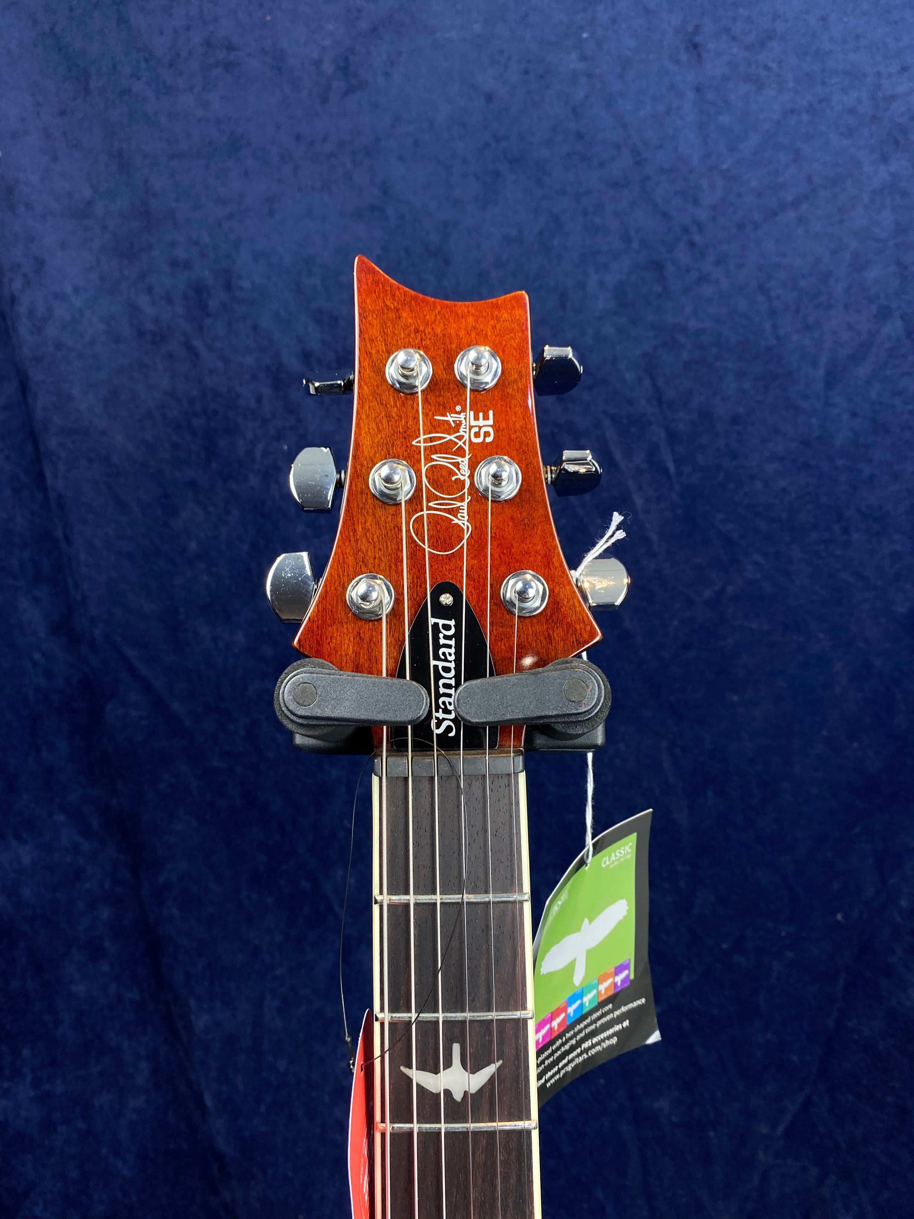 PRS SE Standard electric guitar headstock with a wood finish, six chrome tuning pegs, inlaid logo, and a bird inlay on the dark fretboard.