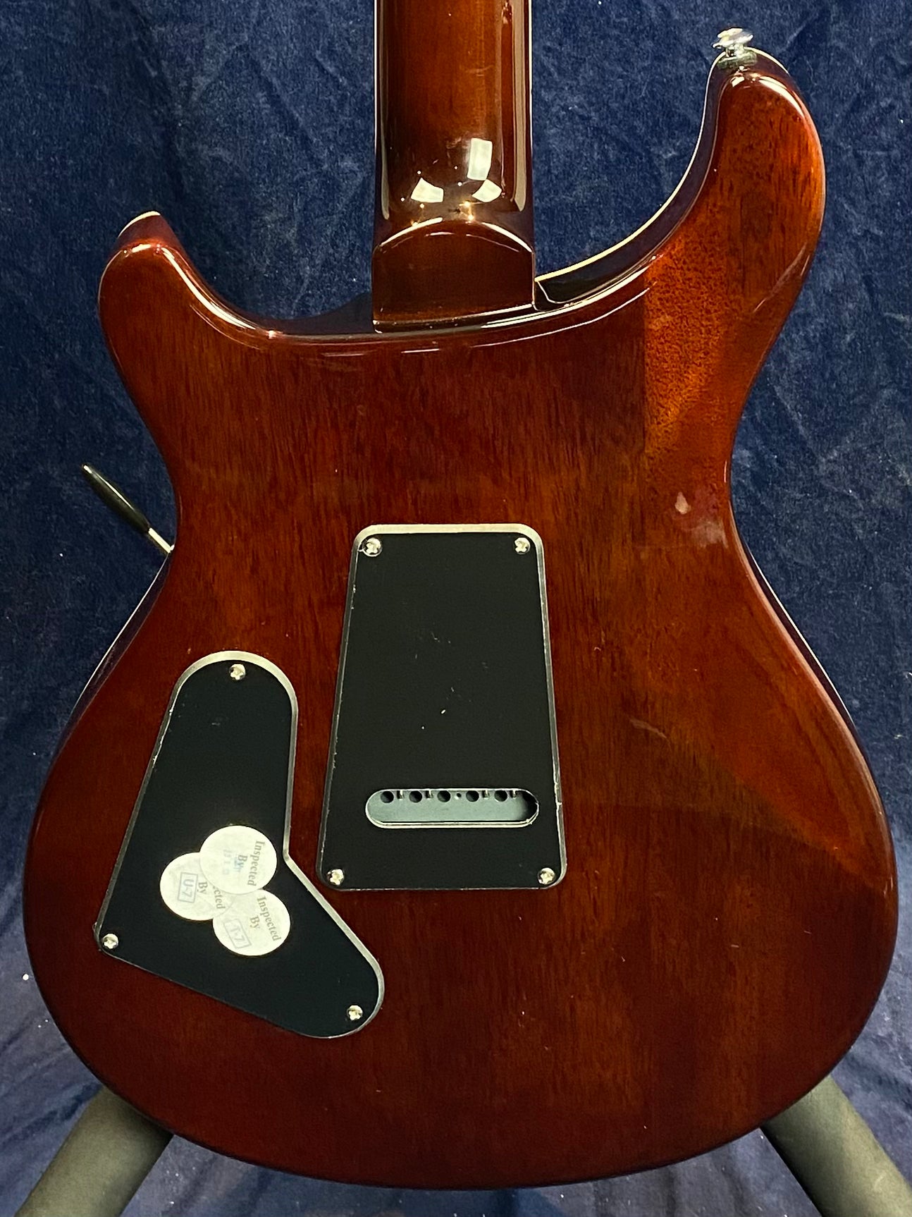 Back of a brown electric guitar showing two black plastic plates with screws and inspection stickers on the lower plate.