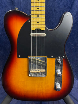 Sunburst electric guitar with a black pickguard, chrome control knobs, and visible wood grain lines on the body.