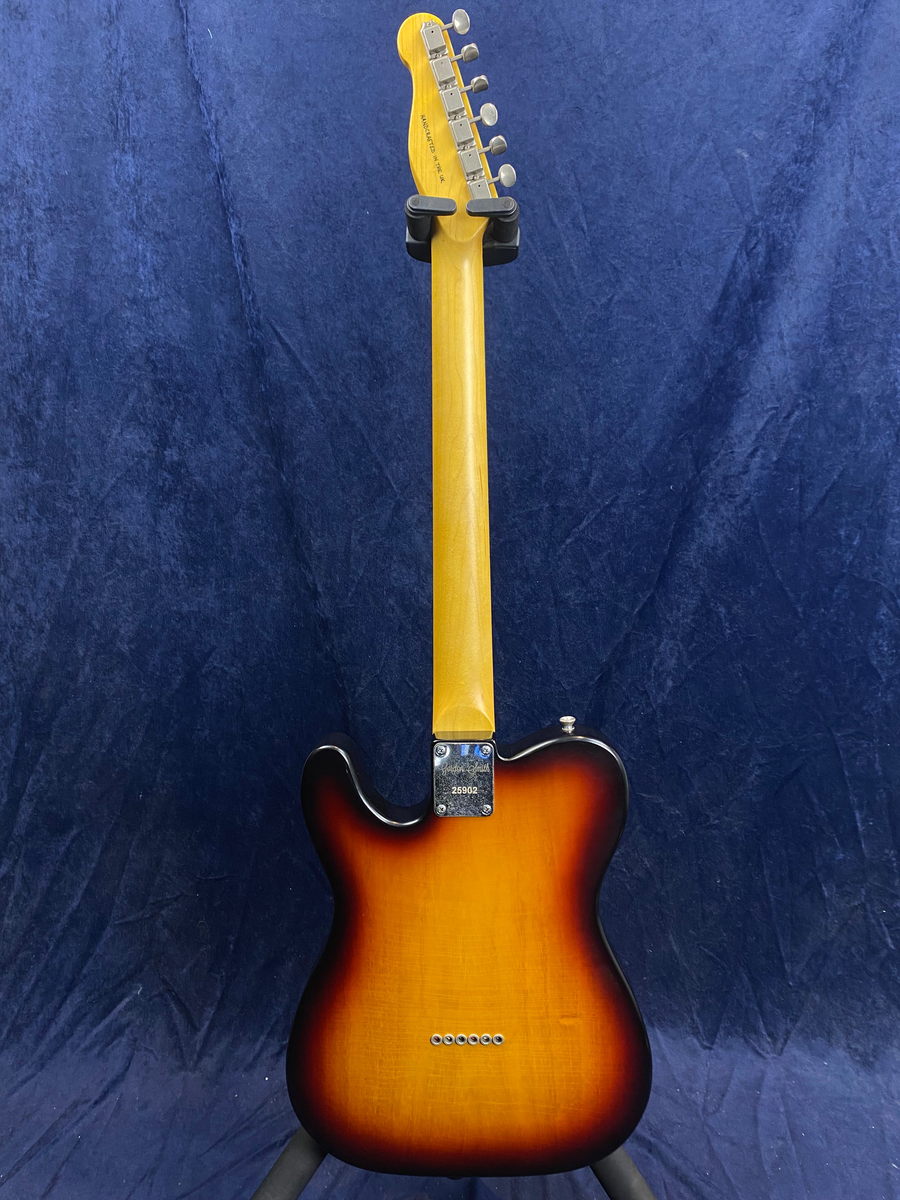 Sunburst electric guitar shown from the back; light wood neck, chrome neck plate, six tuner pegs, and a rounded body with string ferrules visible.