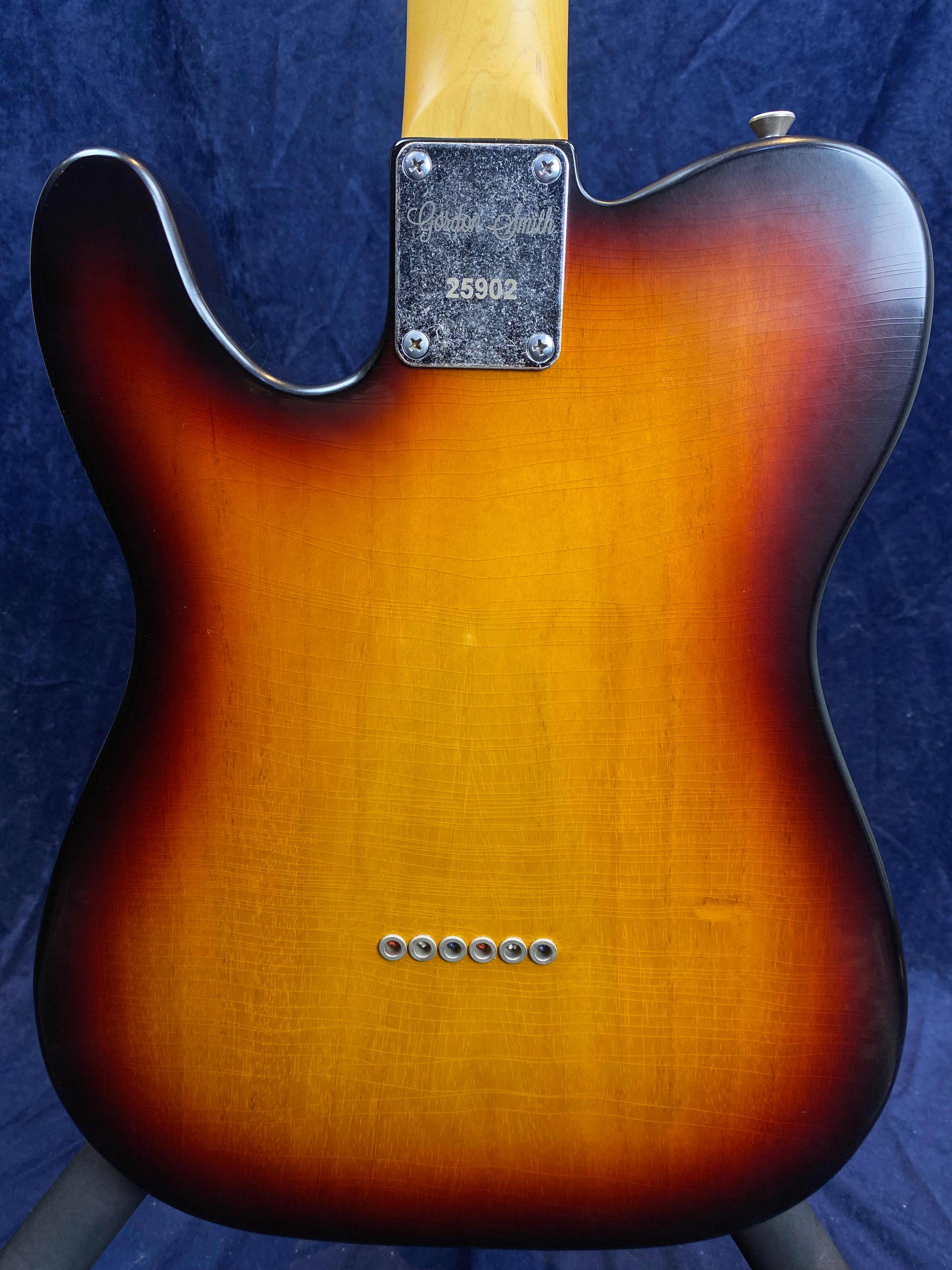 Sunburst finish electric guitar back, visible wood grain, six string ferrules in a row, metal neck plate engraved with "Gordon Smith 25902".