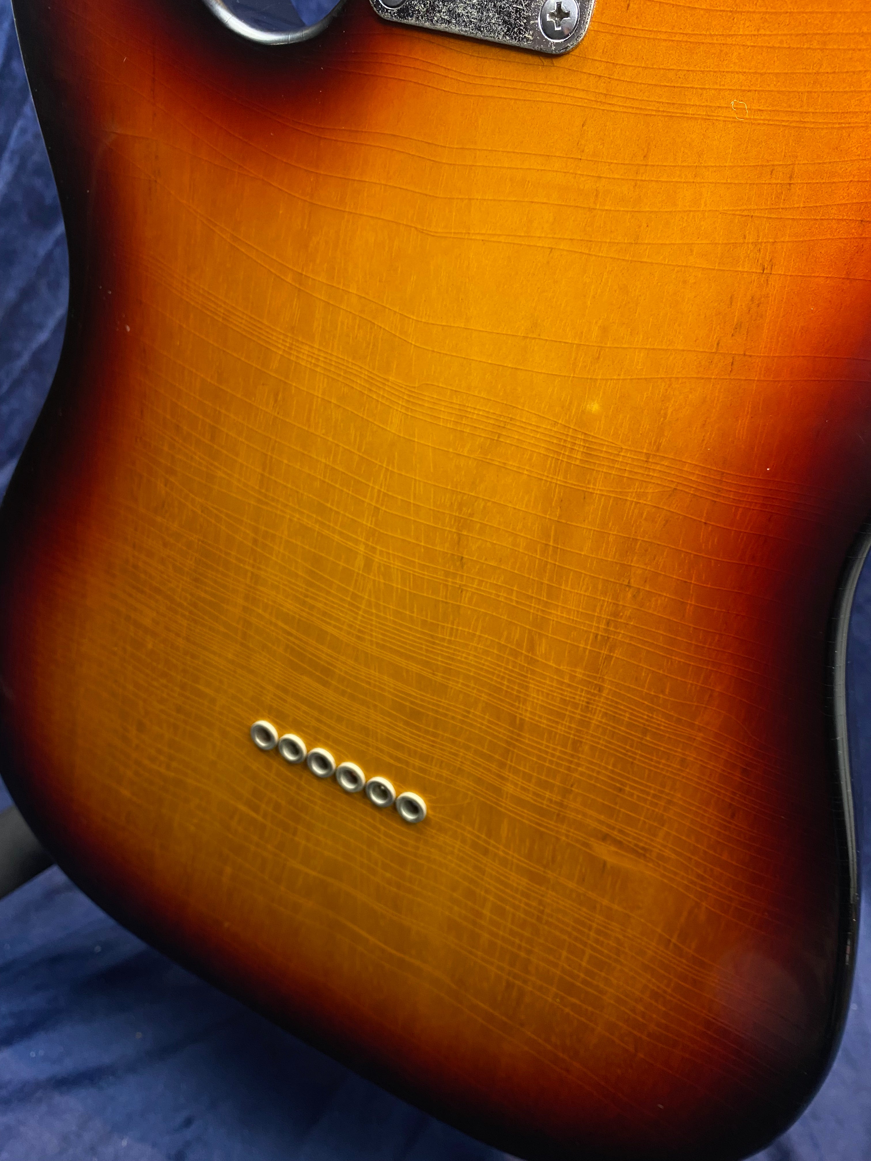Sunburst-finish electric guitar body with visible finish checking and six metal ferrules in a row for string-through design.