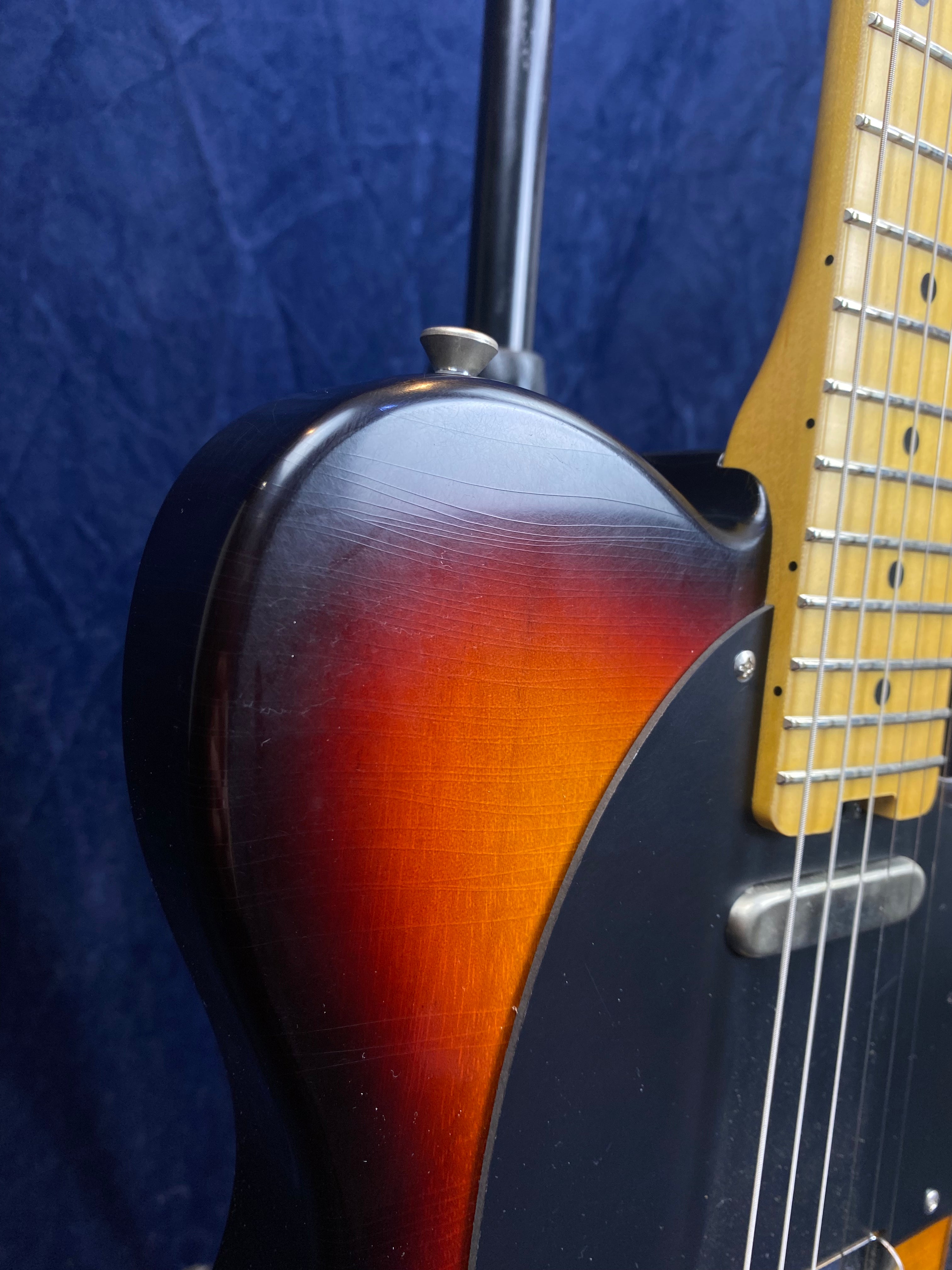 Close-up of a sunburst electric guitar body showing wood grain, fine cracks in the finish, and part of a maple fretboard with metal strings.