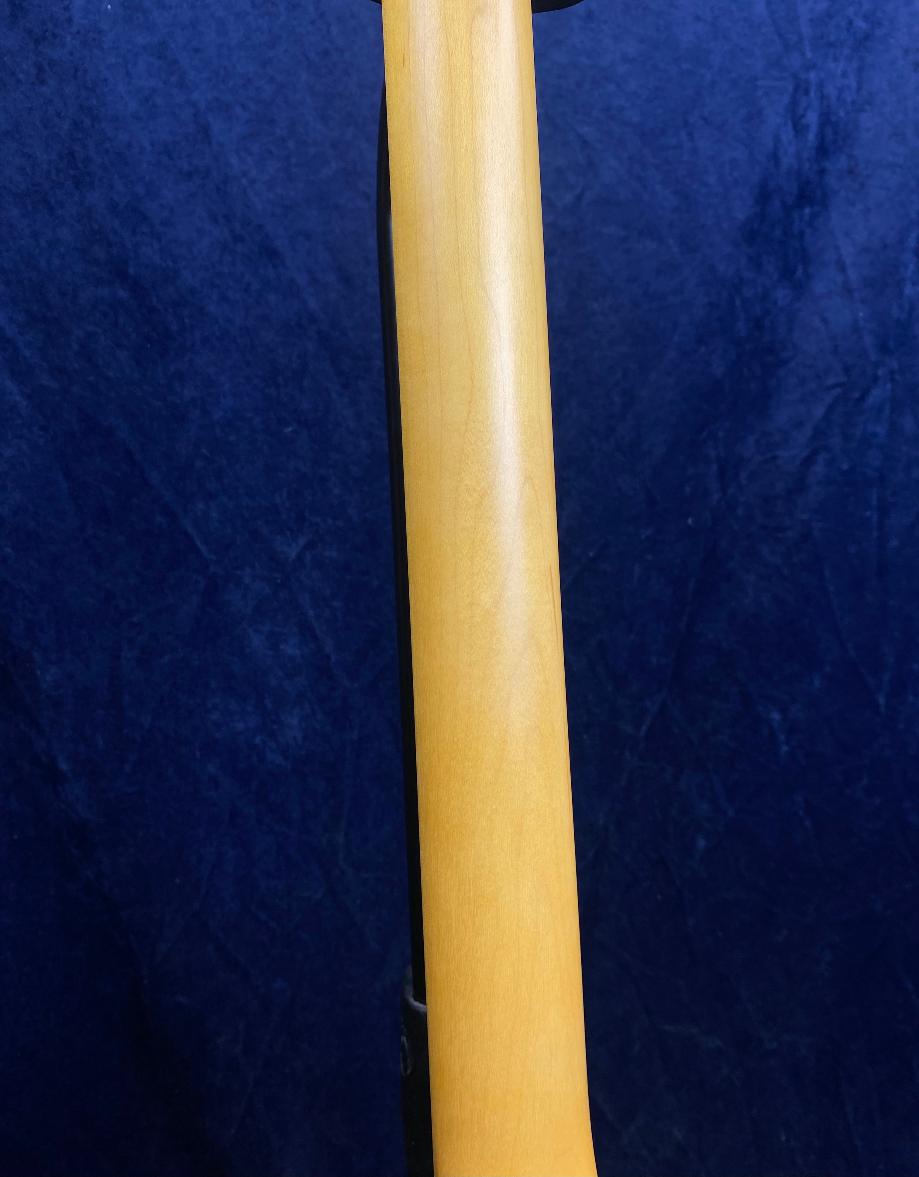 Light wood electric guitar neck shown from the back against a dark blue textured background.