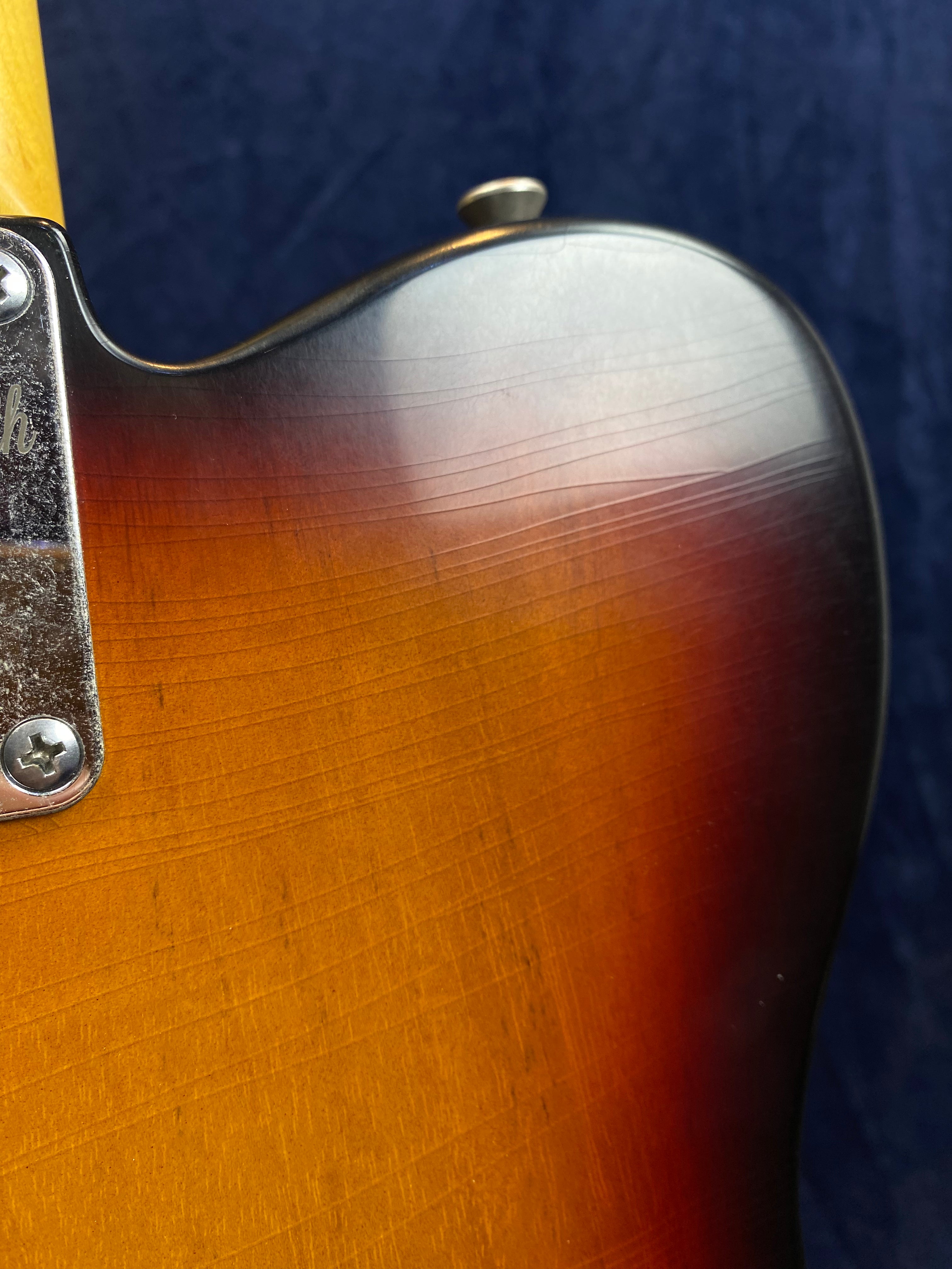 Sunburst electric guitar body close-up with visible lacquer finish cracks, part of the neck joint, and a metal neck plate with screw heads.