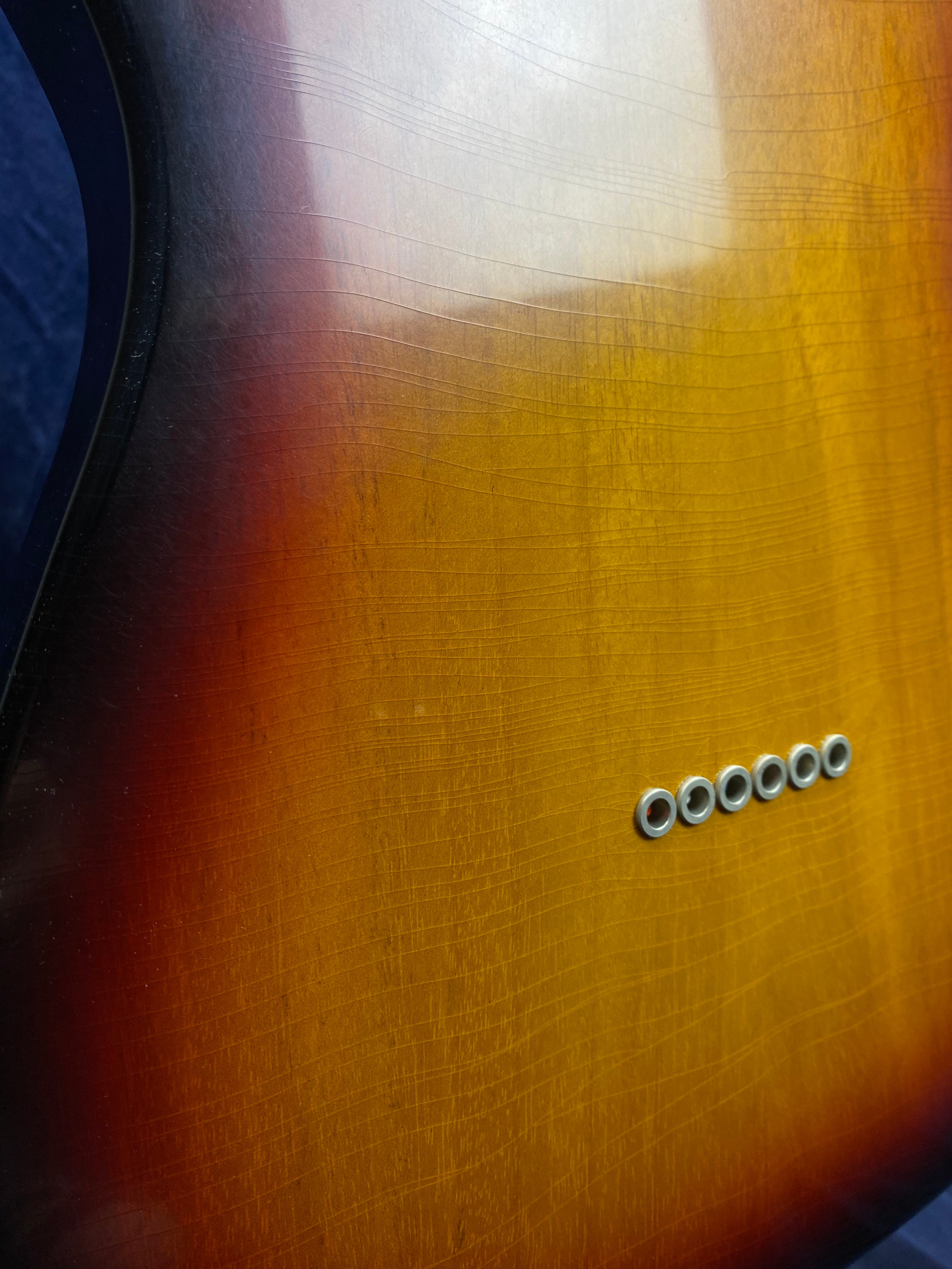 Sunburst finish electric guitar body with visible finish cracks and six metal string ferrules arranged in a row.