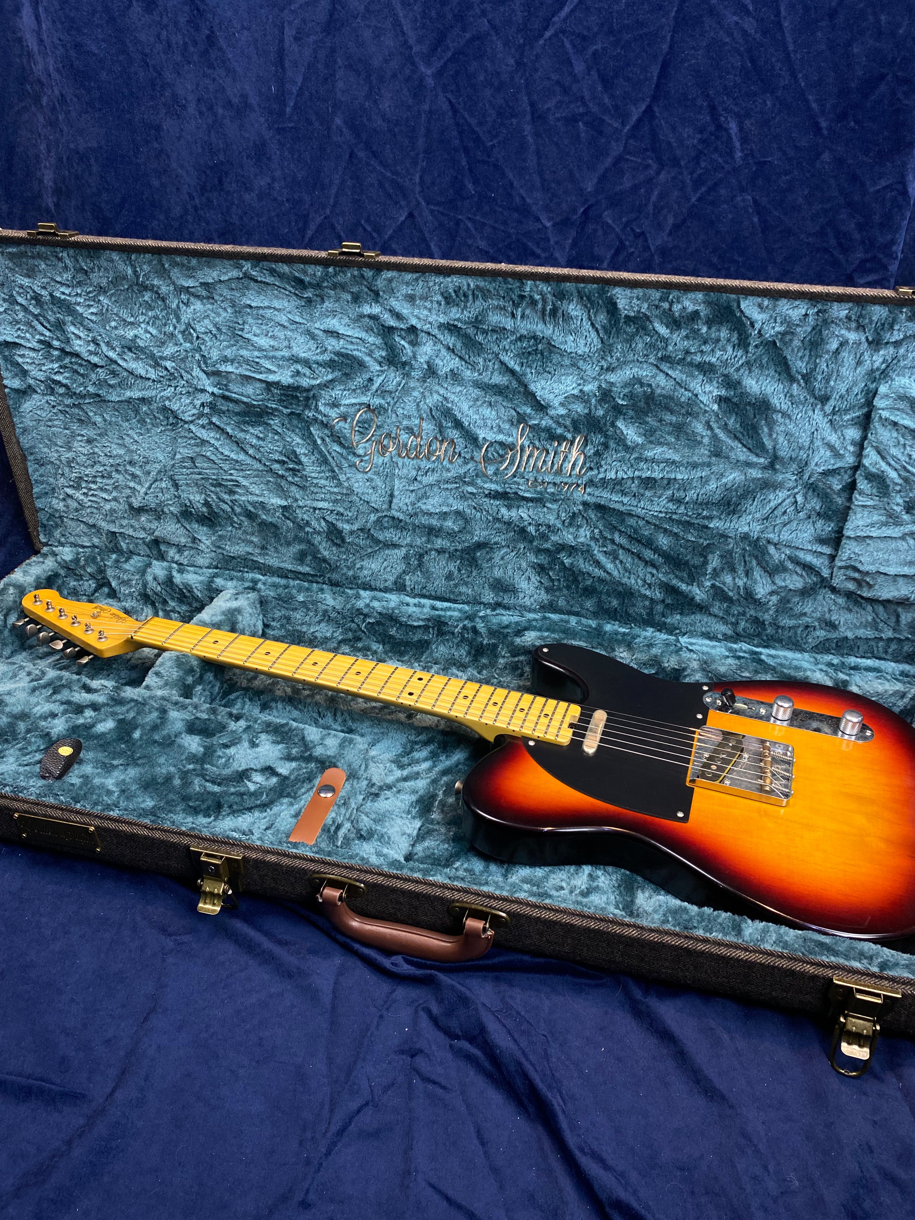 Sunburst electric guitar with black pickguard in a blue velvet-lined Gordon Smith hard case, accessories included.