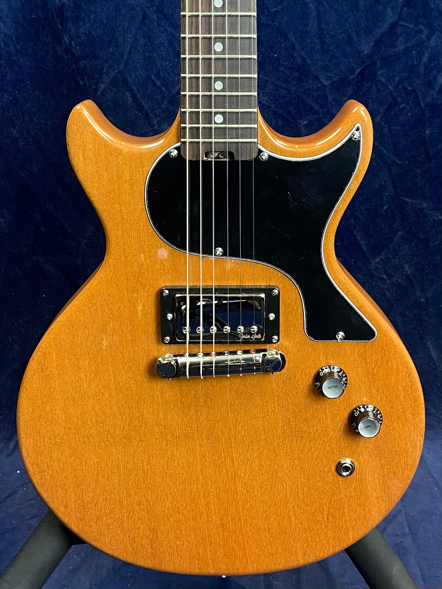 Natural wood finish electric guitar with double cutaway body, single black pickup, three control knobs, and a large black pickguard.