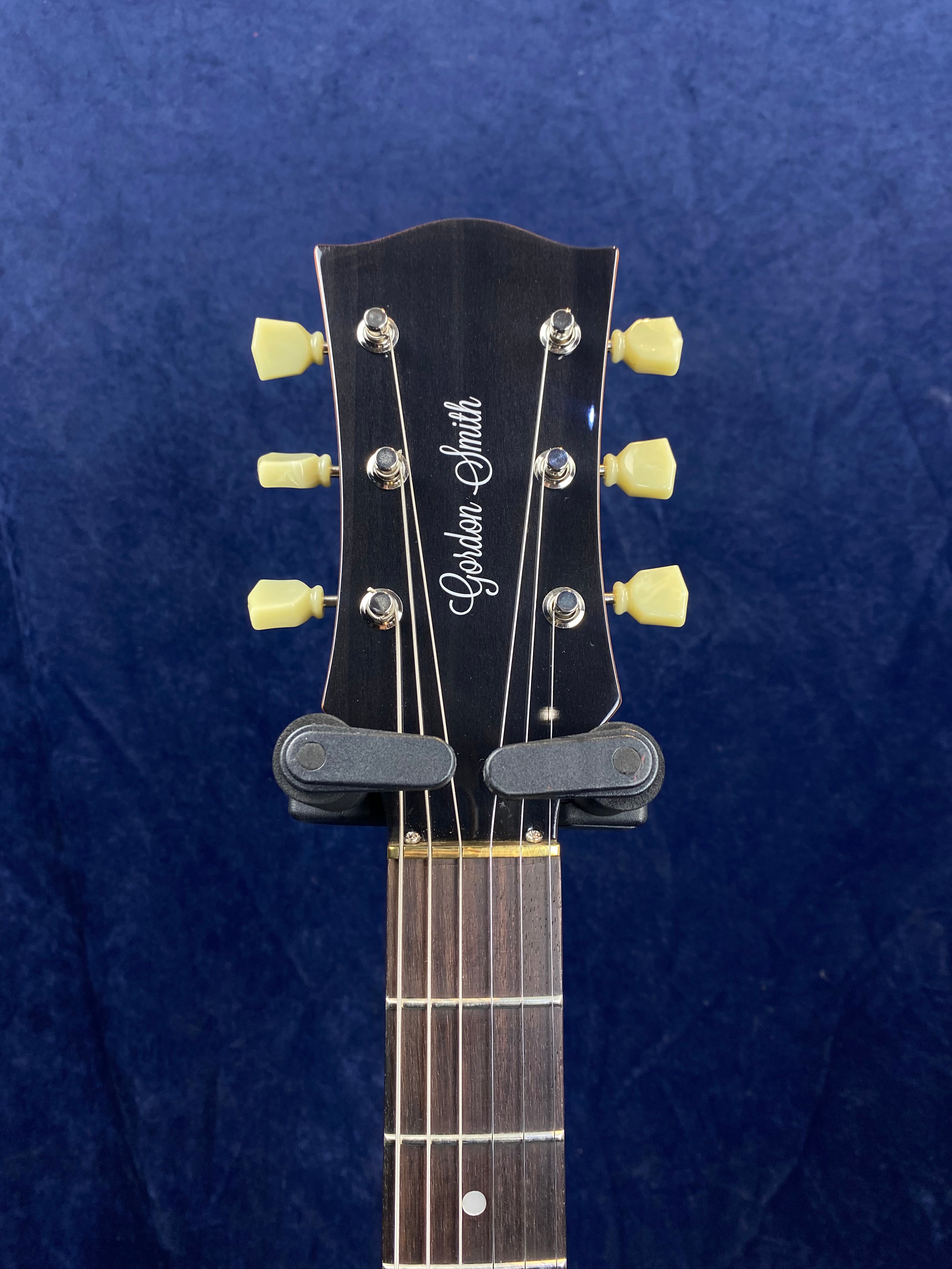 Gordon Smith electric guitar headstock with six cream tuning pegs, black faceplate, and two capos clipped just above the nut.