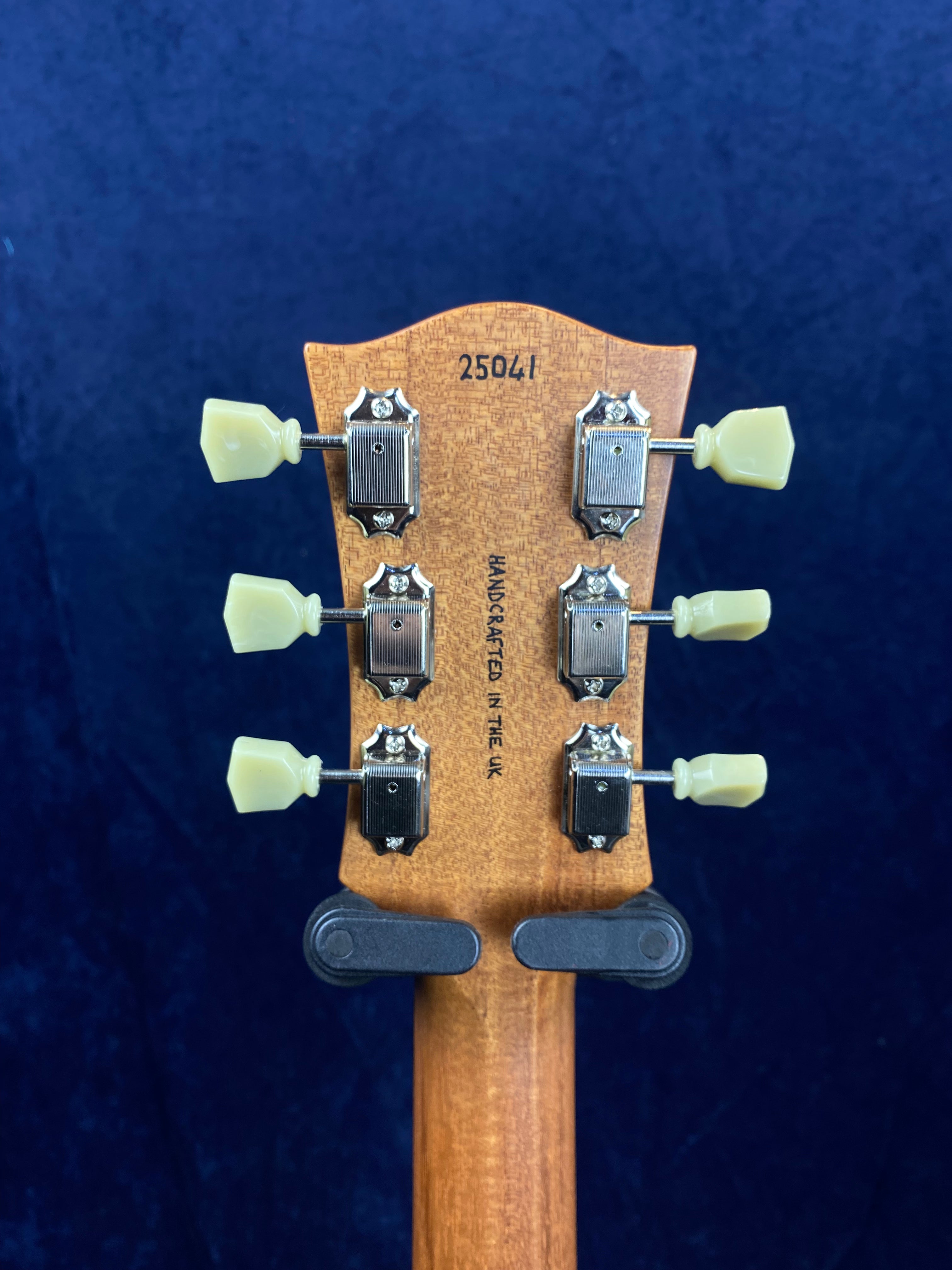 Electric guitar headstock with six vintage-style tuning pegs, serial number 25041, and "Handcrafted in the UK" text on natural wood.