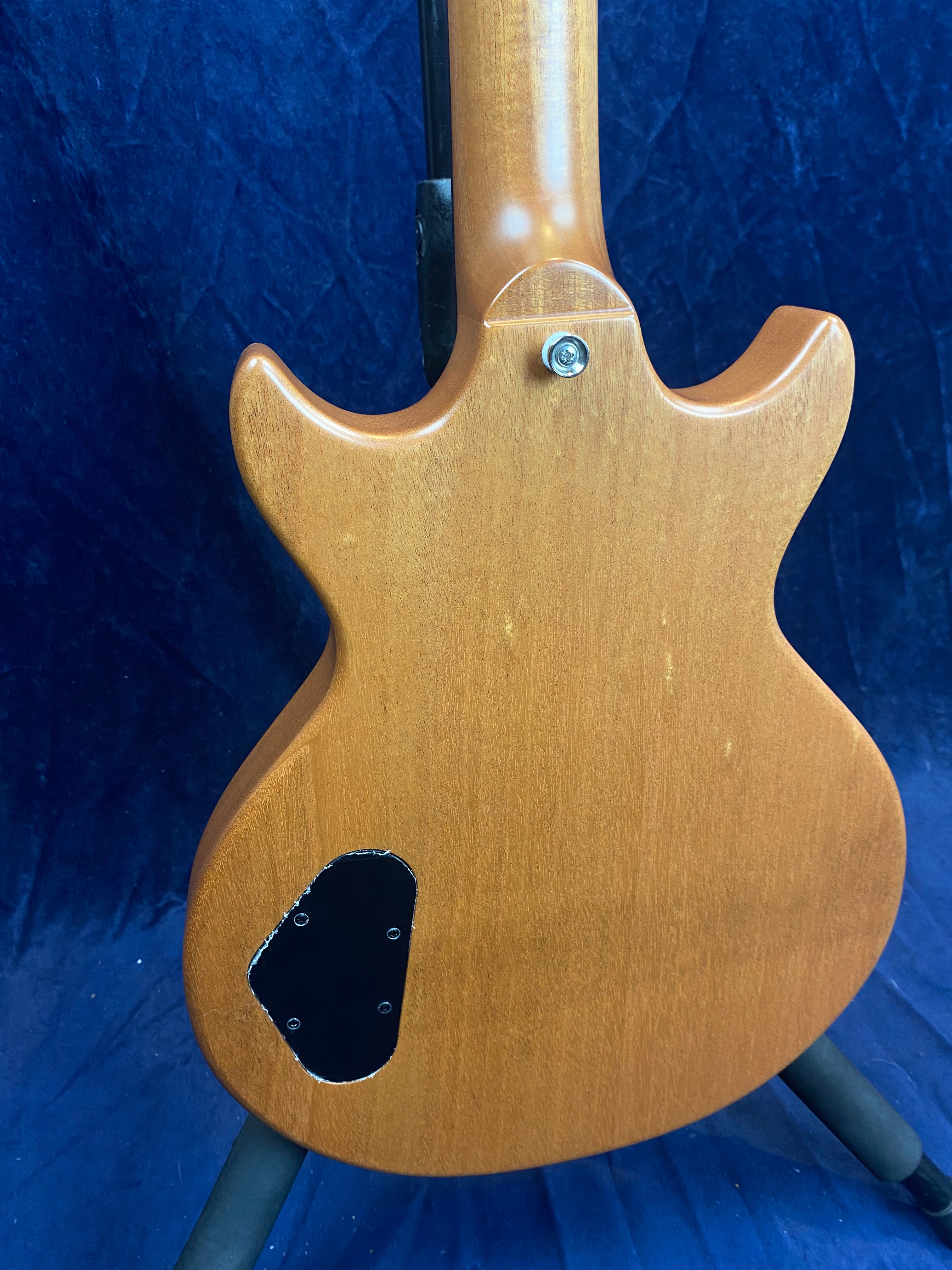Natural wood finish electric guitar back, showing a bolt for a strap and a black plastic electronics cover on the lower left.