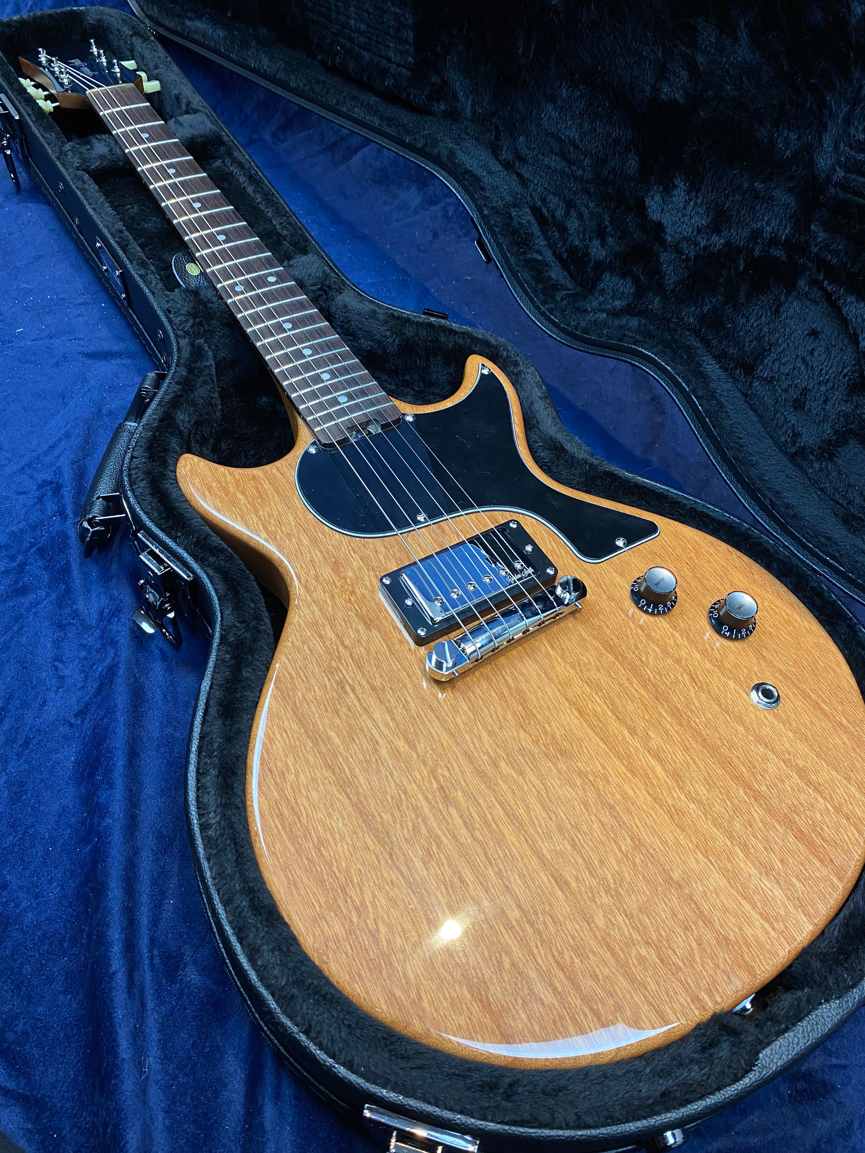 Light brown electric guitar with a black pickguard, two control knobs, and a single pickup, resting in a fitted black case.
