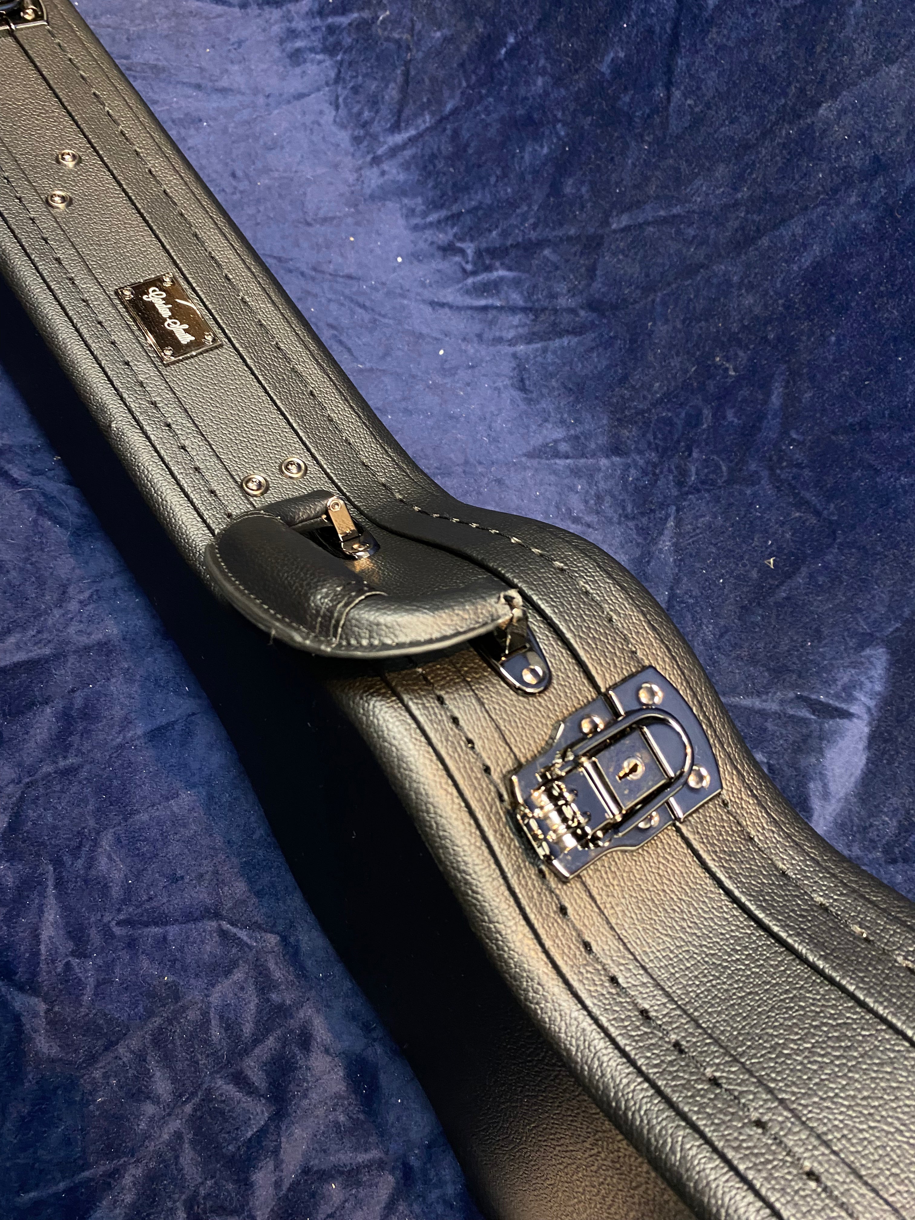 Black hard electric guitar case with chrome latches and a Gibson logo badge, resting on a dark blue textured surface.