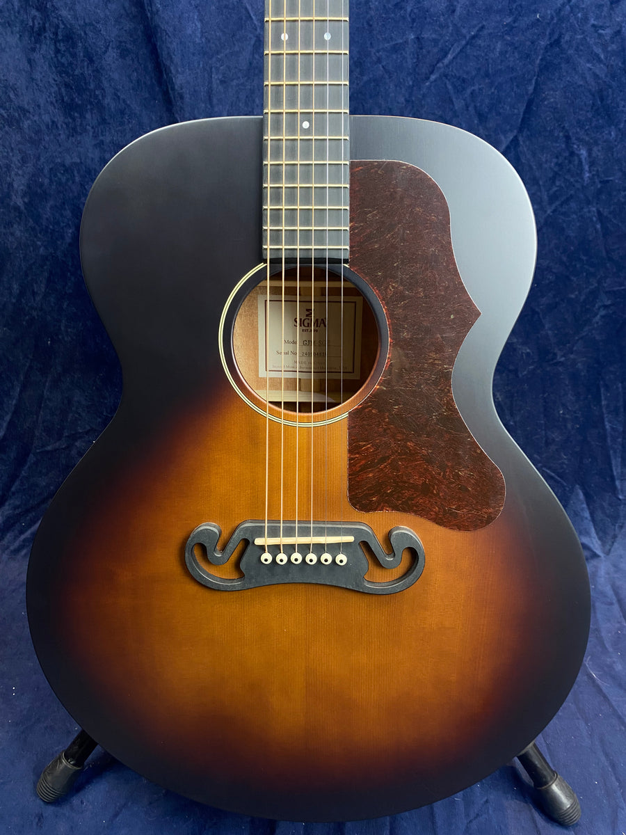 Sunburst acoustic guitar with a large, rounded body, ornate black bridge, tortoiseshell pickguard, and cream ring around the sound hole.