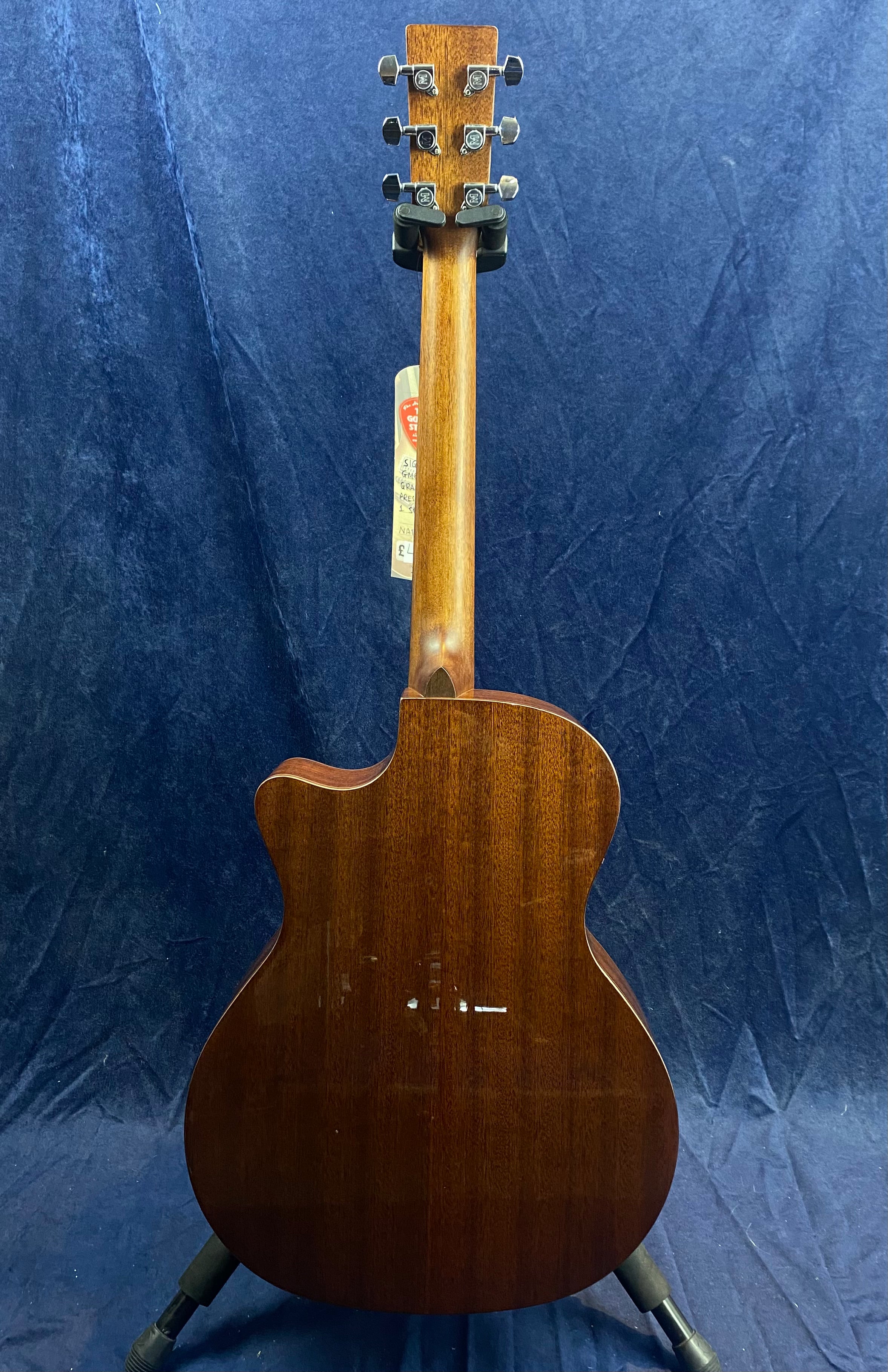 Acoustic guitar with a glossy dark wood back, cutaway body shape, and six tuning pegs, shown from the rear against a dark blue background.
