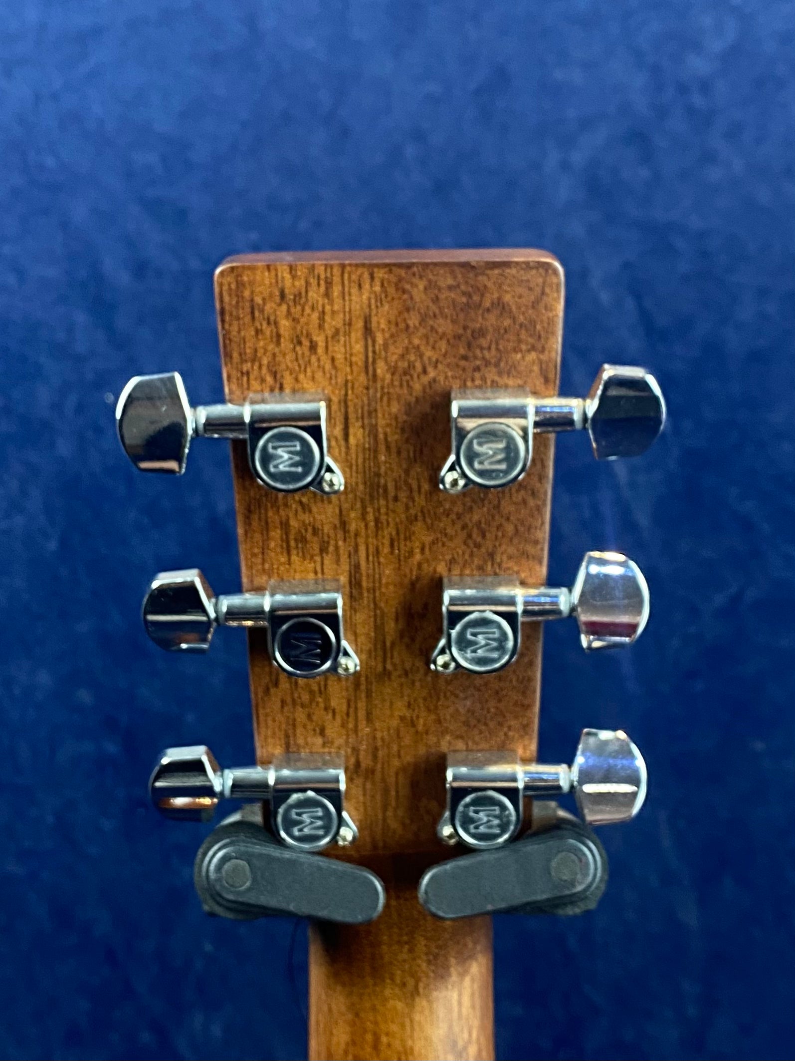 Six chrome tuning pegs with "W" logos are mounted on the wooden headstock of an acoustic guitar, with two black strap lock mechanisms at the bottom.