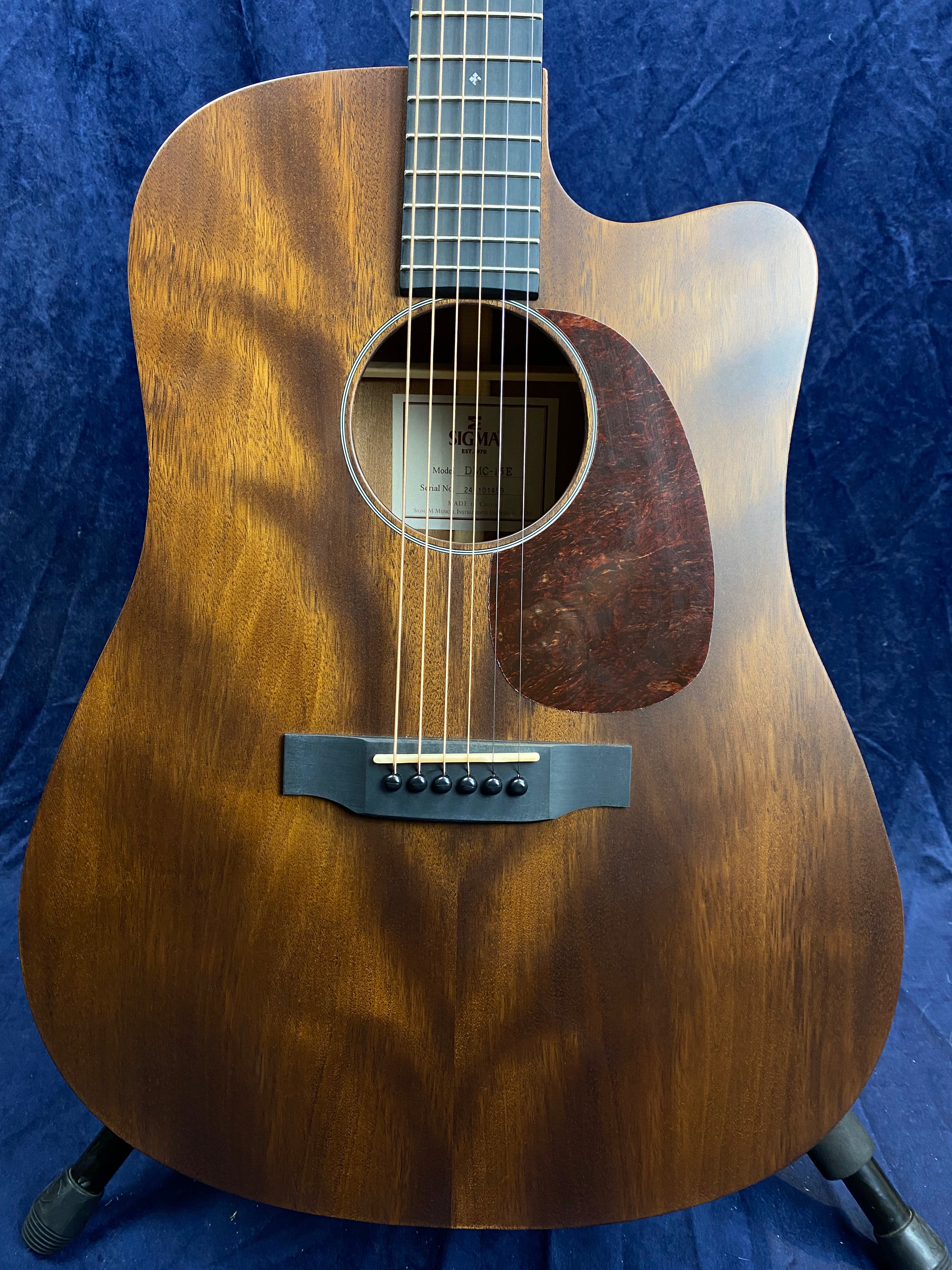Dreadnought acoustic guitar with a cutaway, matte brown wood finish, dark tortoiseshell pickguard, and six steel strings against a dark blue background.