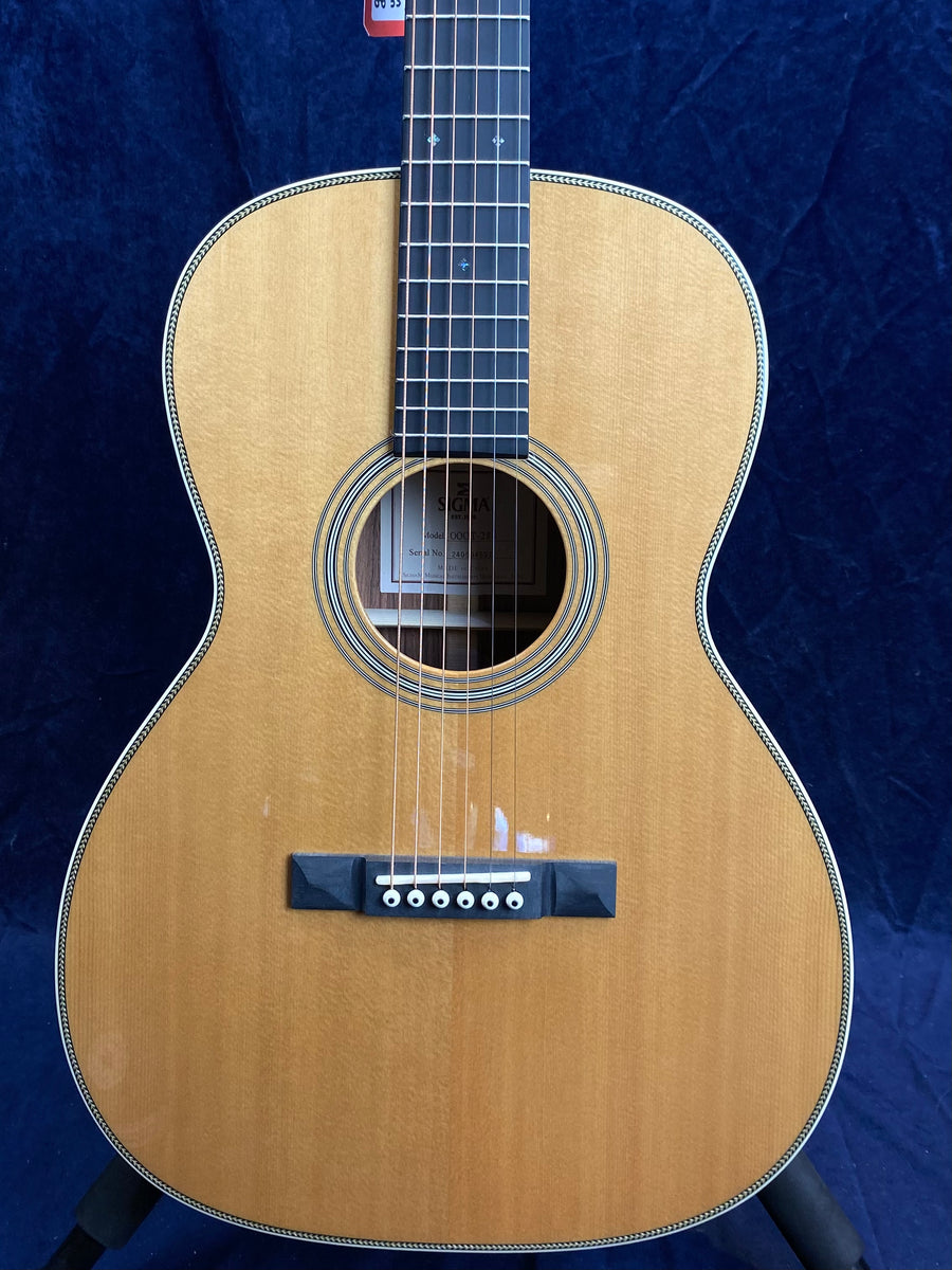 Natural wood acoustic guitar with a dark fretboard, six strings, and a simple rosette around the sound hole, shown against a dark blue background.