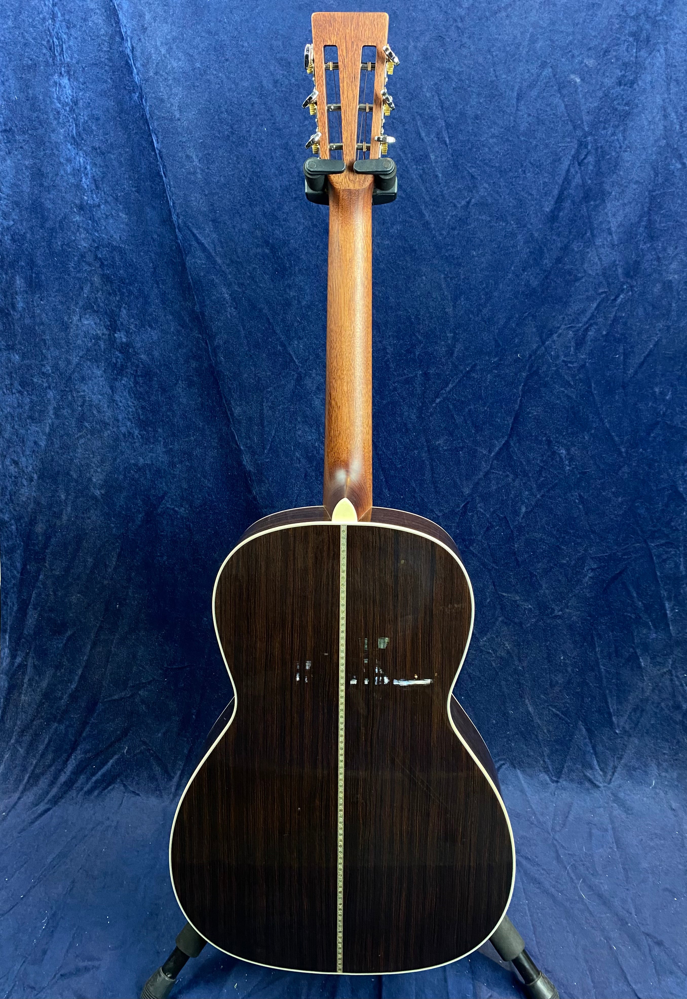 Acoustic guitar shown from the back, featuring dark glossy wood with a light decorative center strip and cream binding along the body edges.