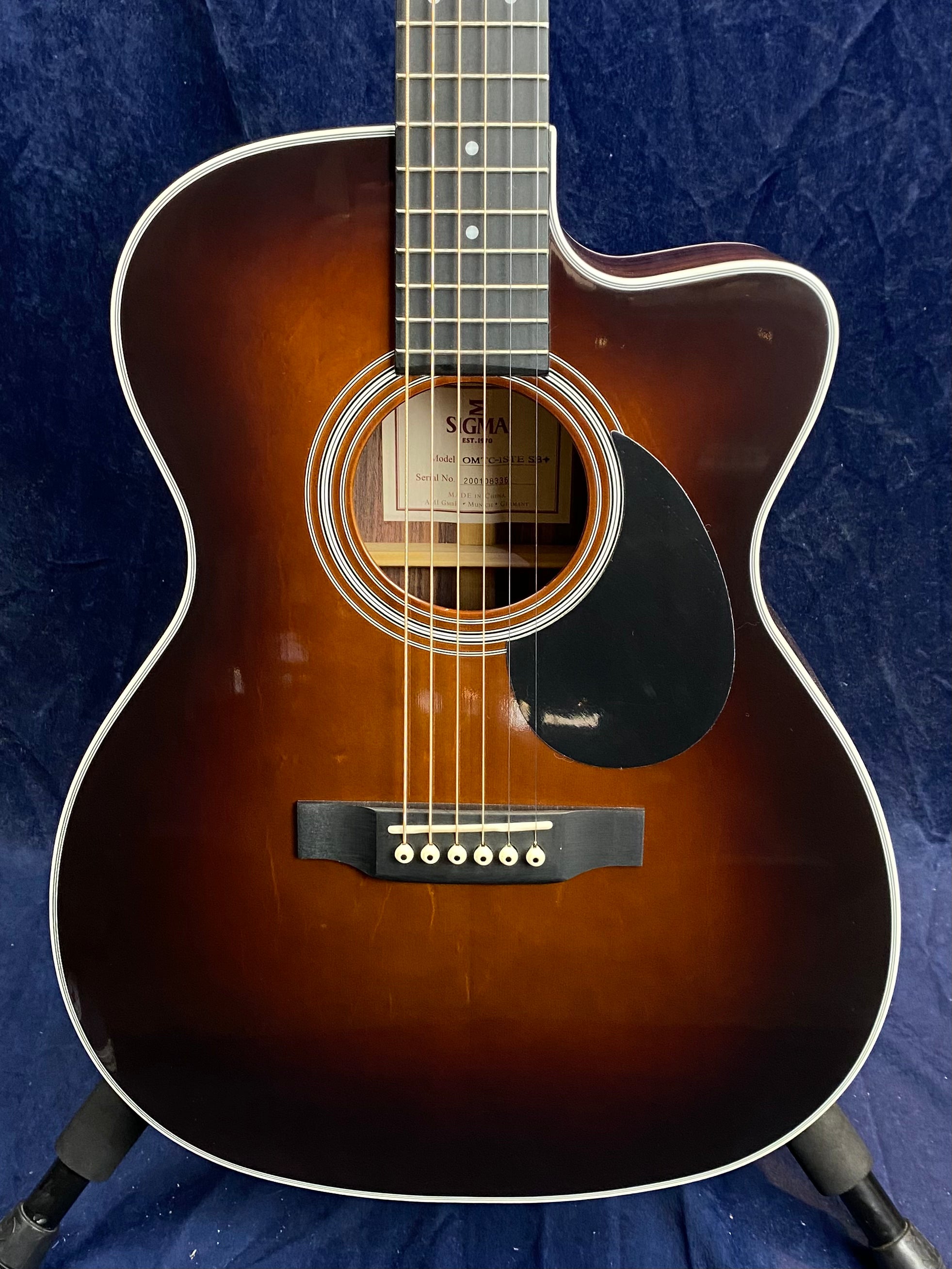 Sunburst finish acoustic guitar with a cutaway body, six strings, white binding, black pickguard, and a rosette around the sound hole.