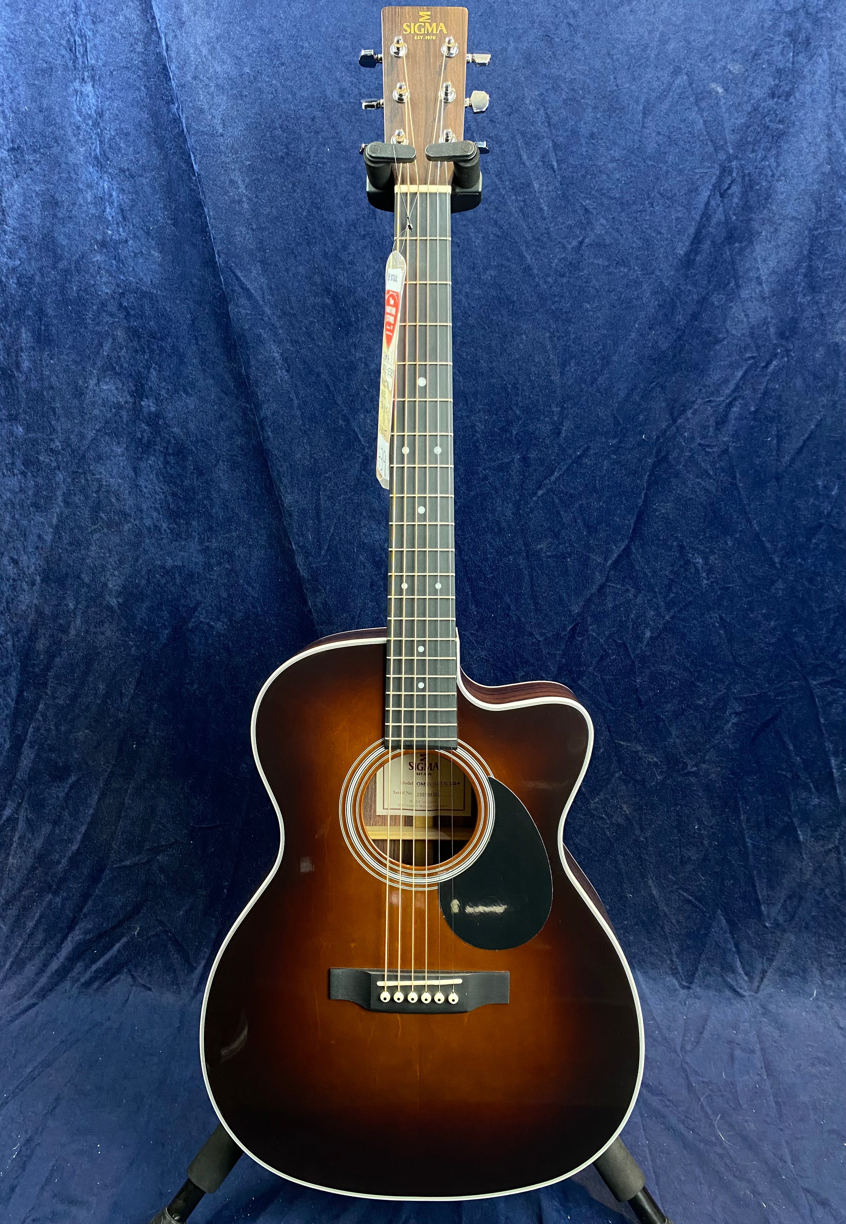 Sigma acoustic guitar with a dark sunburst finish, white trim, cutaway body, black pickguard, six strings, and dot inlays on the fretboard.
