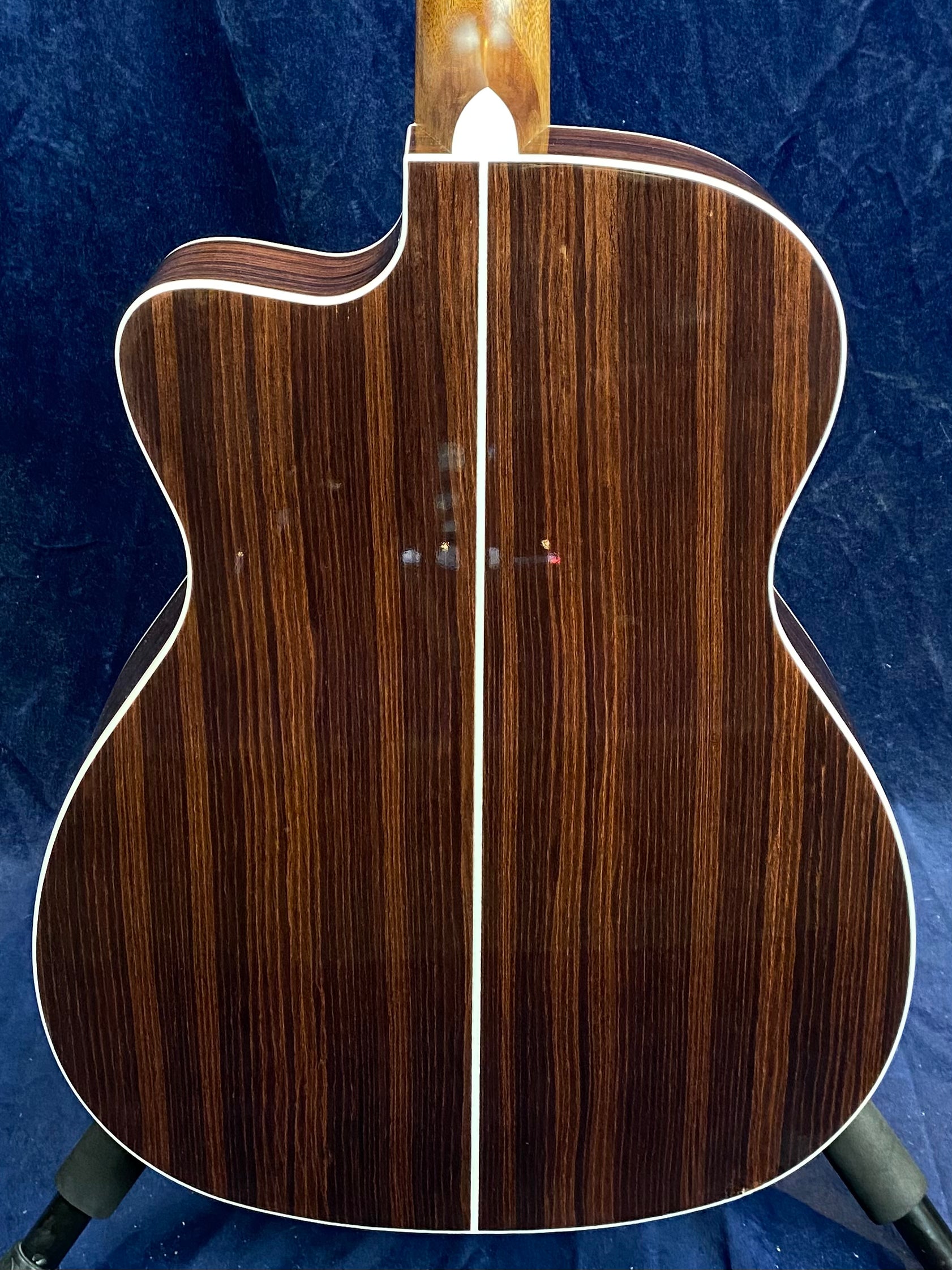 Back of an acoustic guitar with dark wood and lighter vertical grain, white binding edges, and a single light center stripe dividing the back.