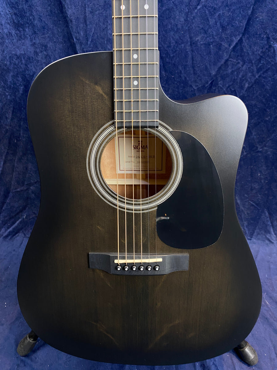 Matte black acoustic guitar with a cutaway design, six strings, circular sound hole with concentric rings, and a black pickguard on the right.