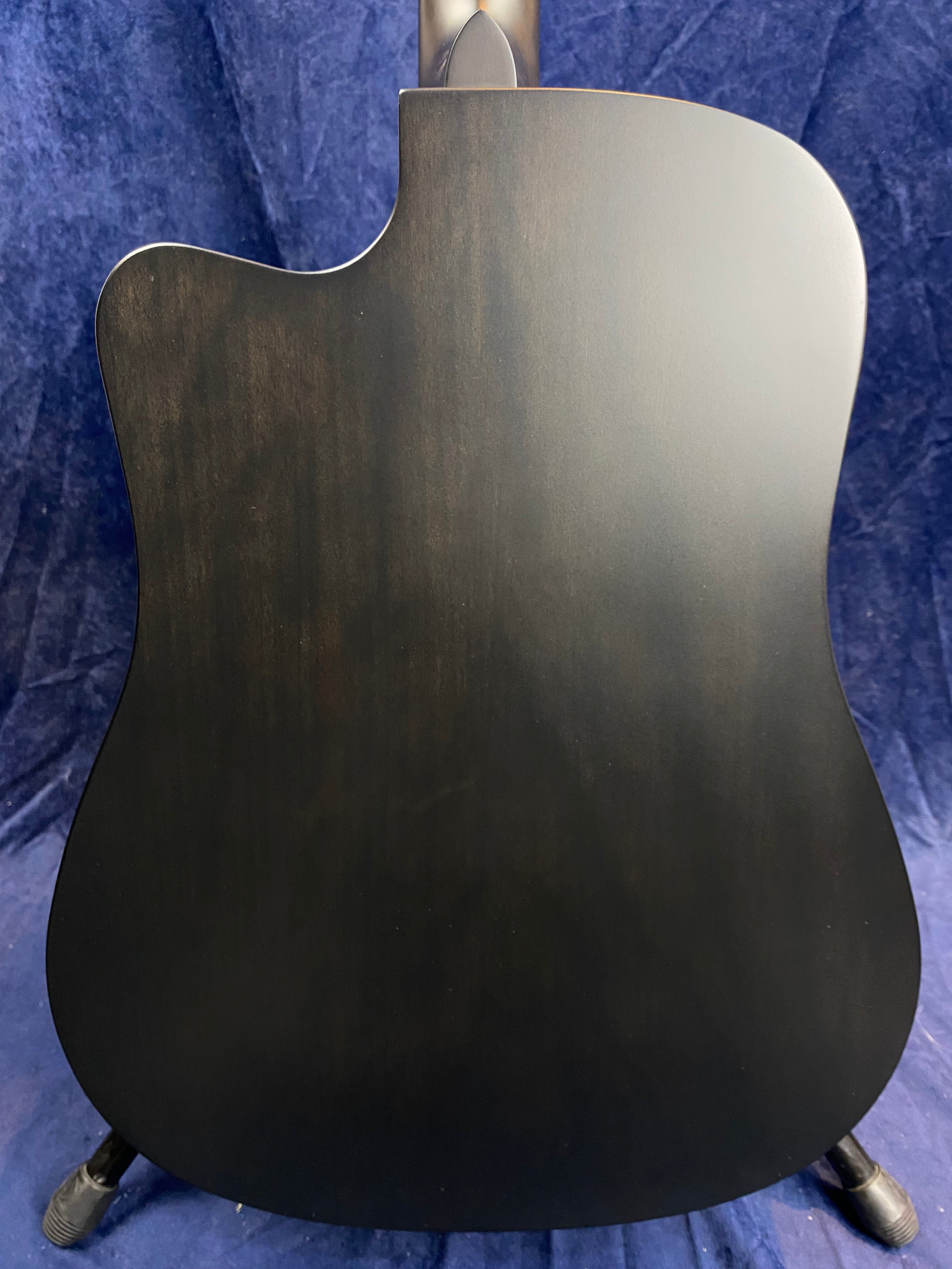 The back of an acoustic guitar with a smooth, matte black finish and a cutaway design, shown against a dark blue background.