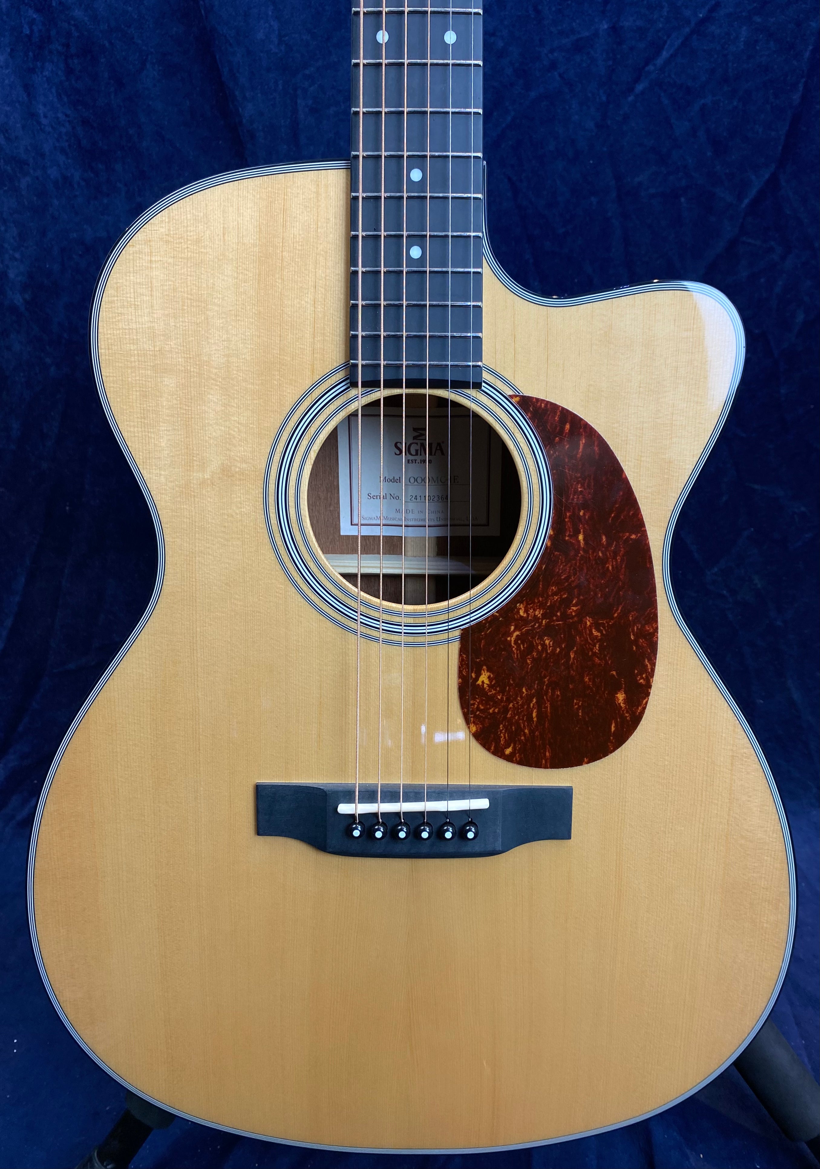 Natural wood acoustic guitar body with a dark tortoiseshell pickguard, six strings, circular sound hole, and black bridge with white pegs.