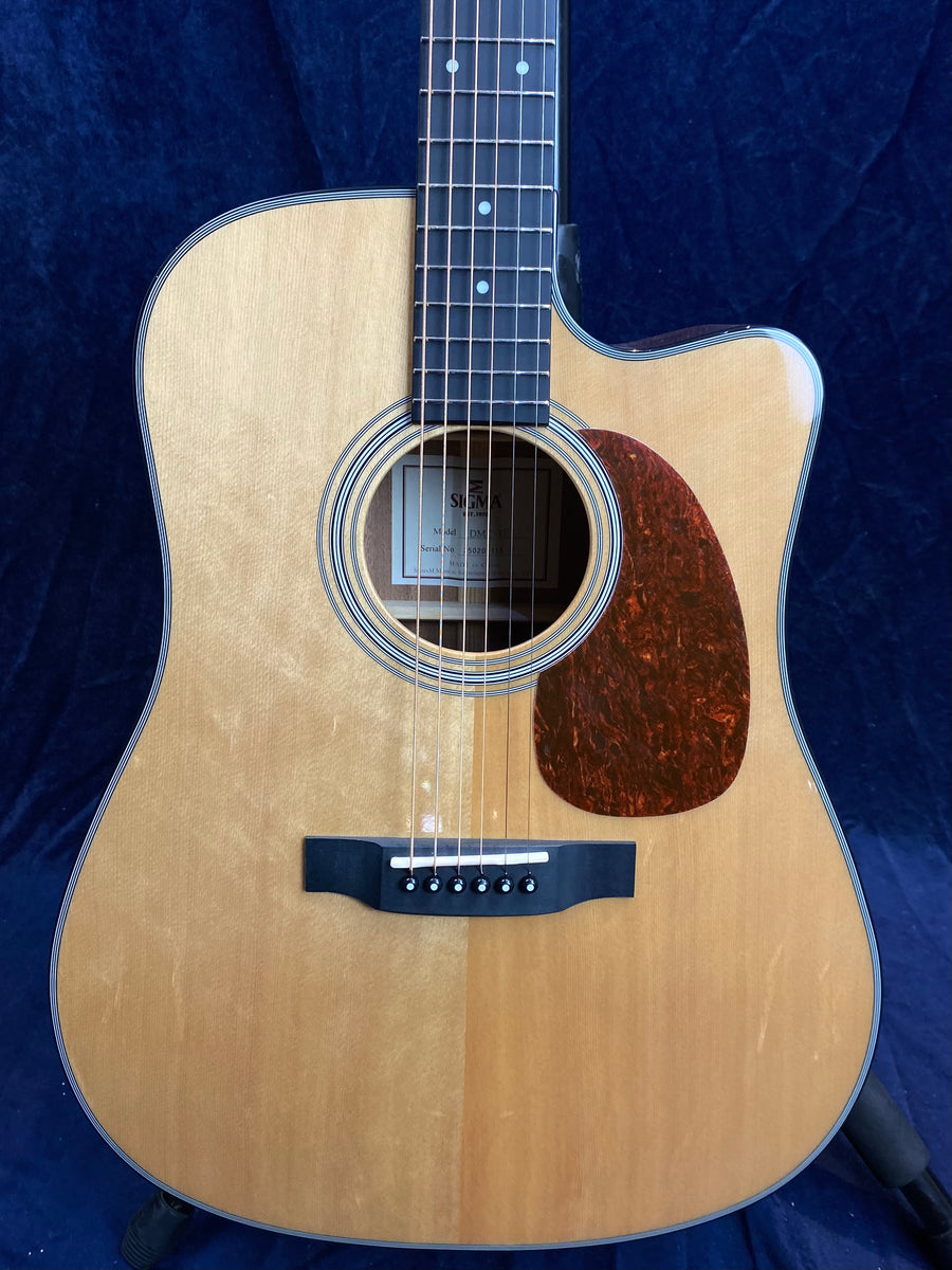 Light wood acoustic guitar with a dark pickguard, six strings, and a single cutaway on the body’s upper right side.