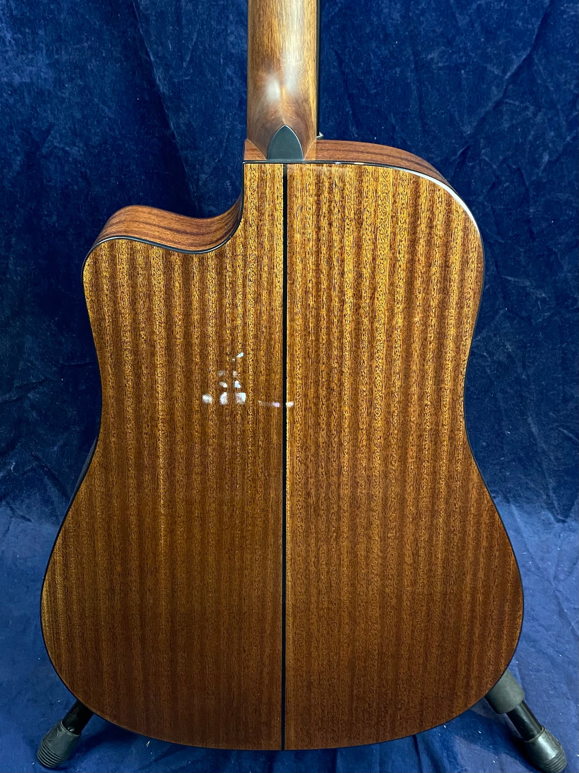 Back of an acoustic guitar with a dark wood grain finish, central seam, minor light scuffs on the left side, and a cutaway near the neck.