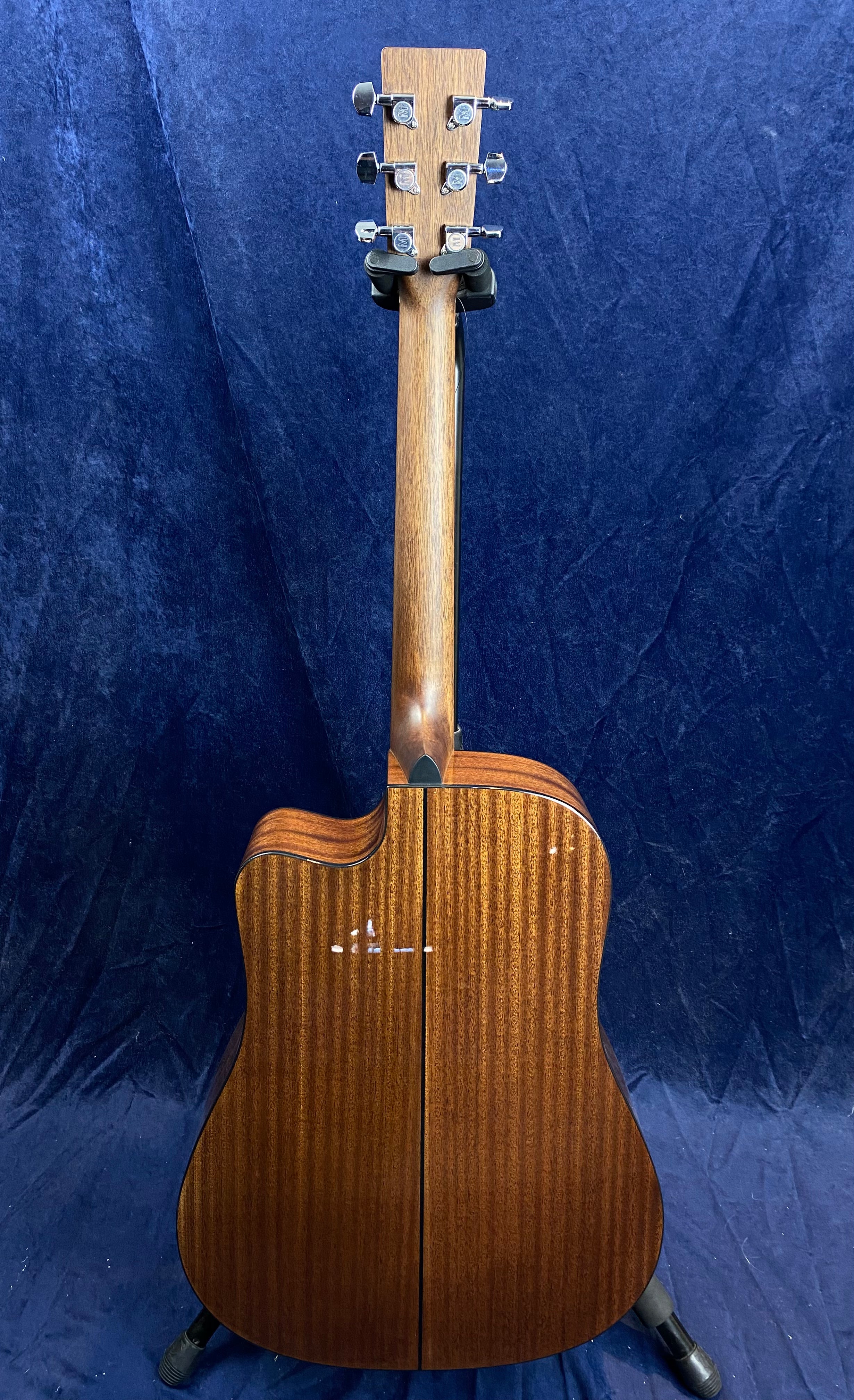 Mahogany acoustic guitar shown from the back, with a glossy striped wood finish, silver tuning pegs, and a cutaway body shape.