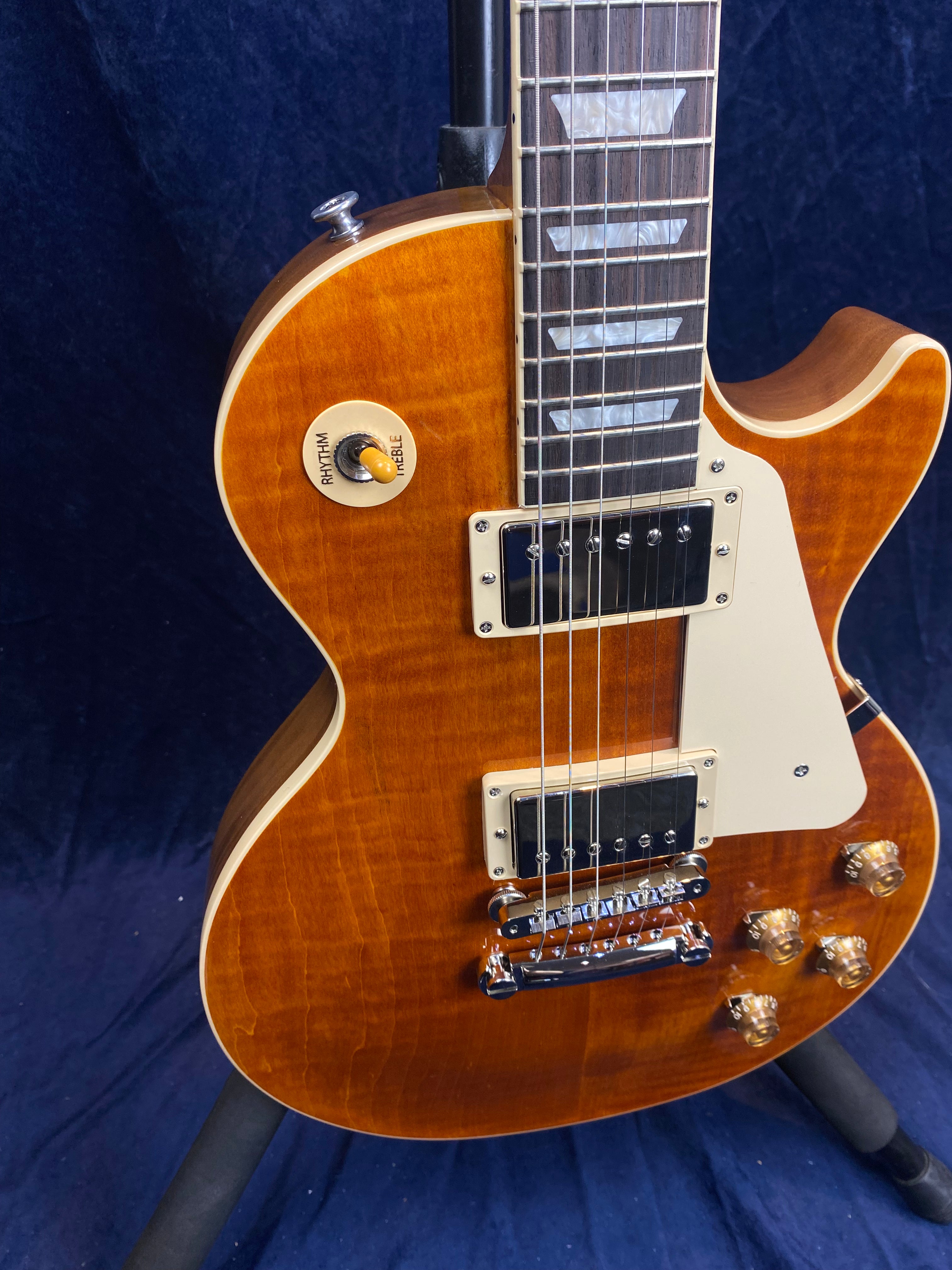 Classic-style electric guitar with a glossy brown finish, cream pickguard, four amber control knobs, and a three-way toggle switch labeled rhythm and treble.