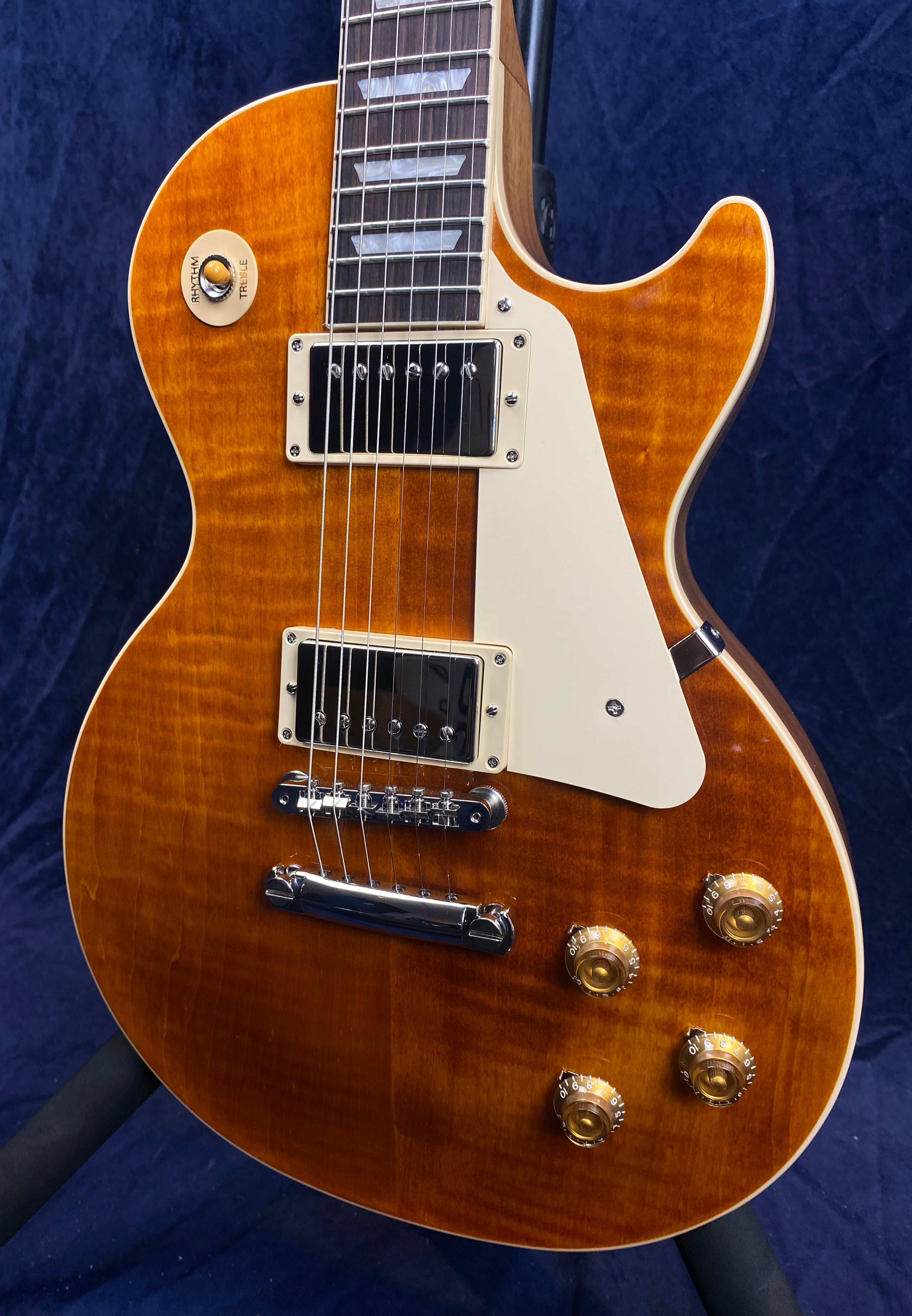 Sunburst electric guitar with cream pickguard, two chrome humbucker pickups, four gold control knobs, and a toggle switch labeled rhythm and treble.