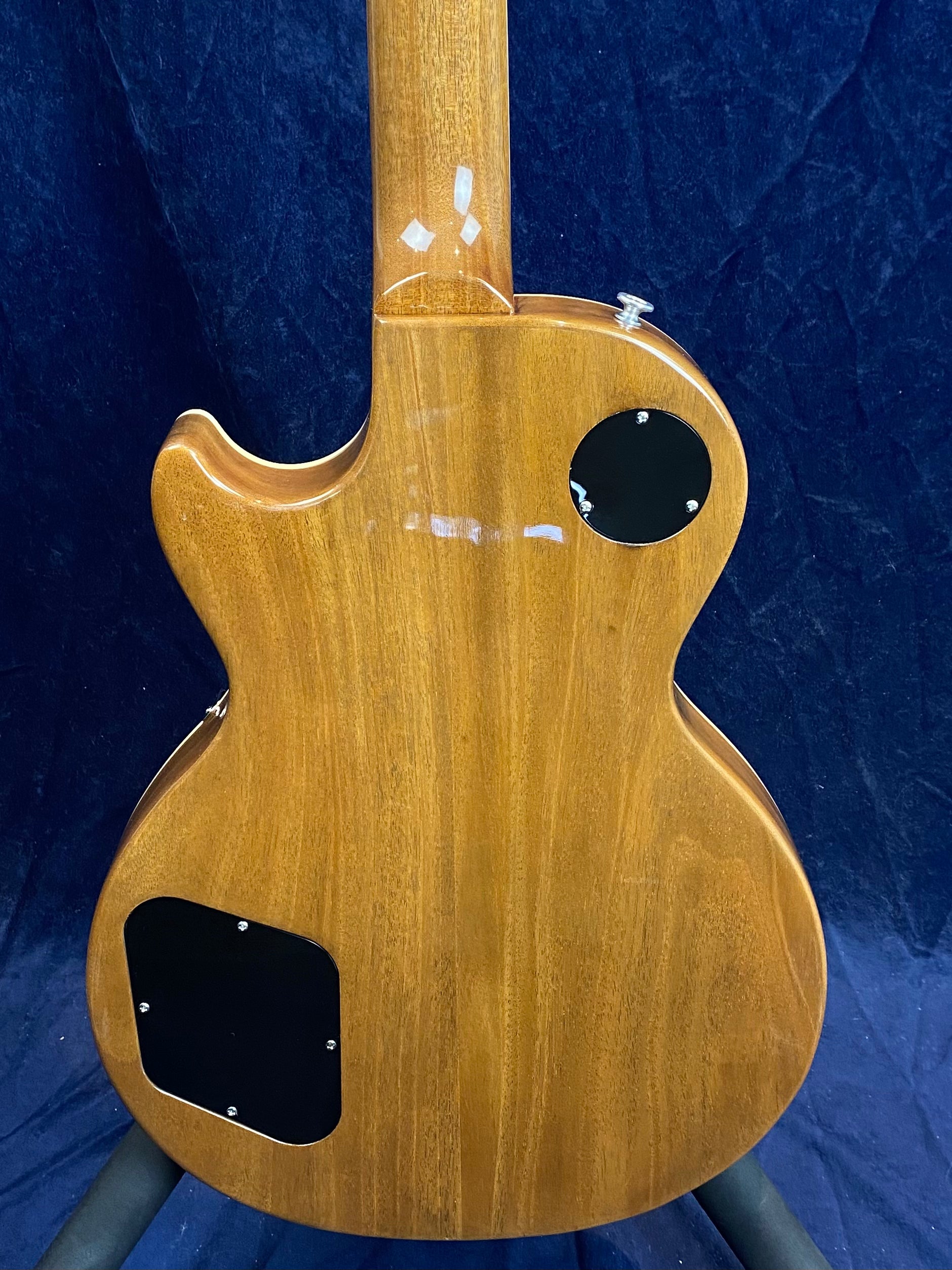 Glossy natural wood electric guitar back with two black plastic cavity covers, rounded single cutaway shape, and visible grain patterns.