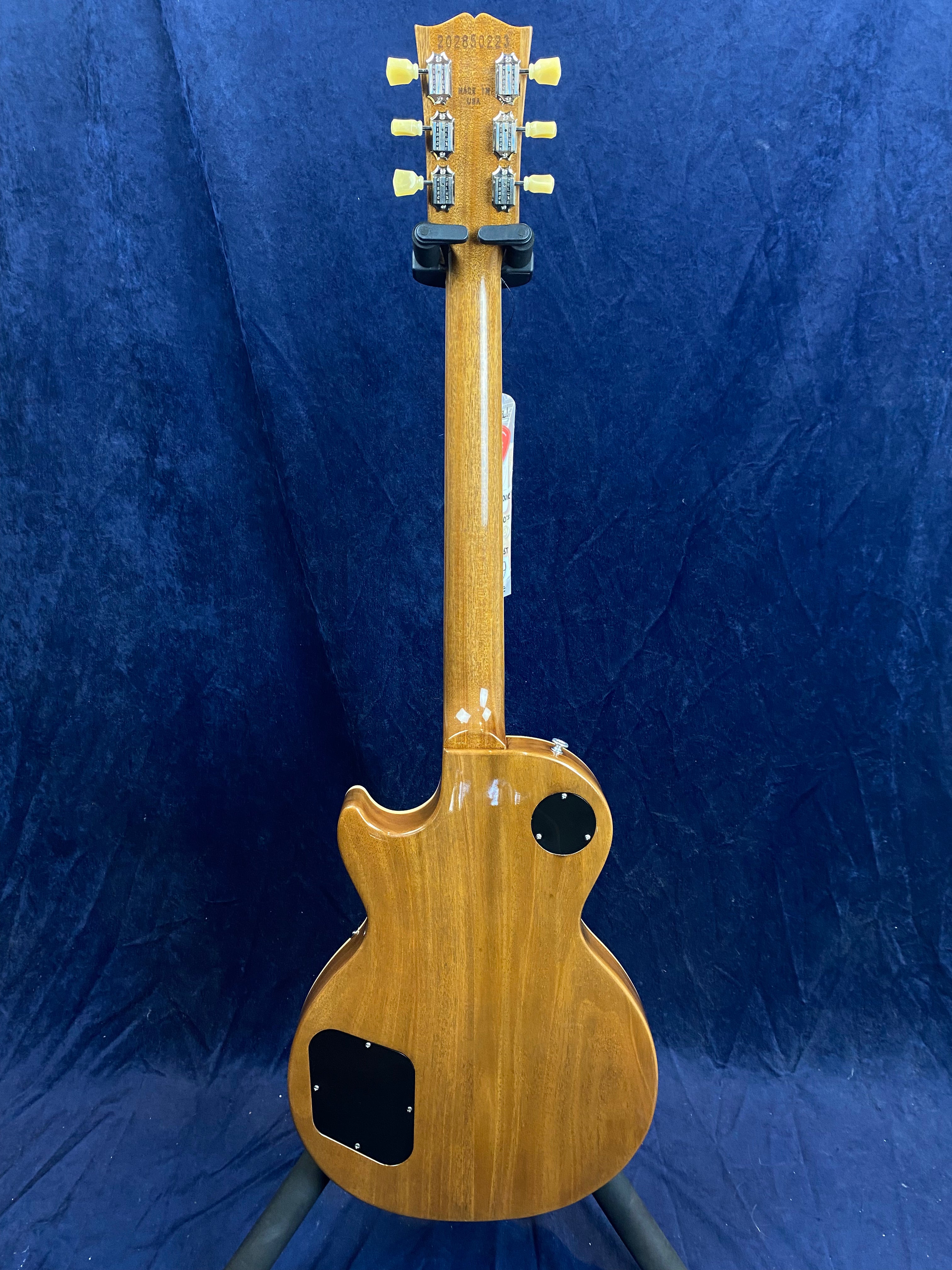 Back view of a single-cutaway electric guitar with a natural wood finish, two black plastic control cavity covers, and six tuners on the headstock.