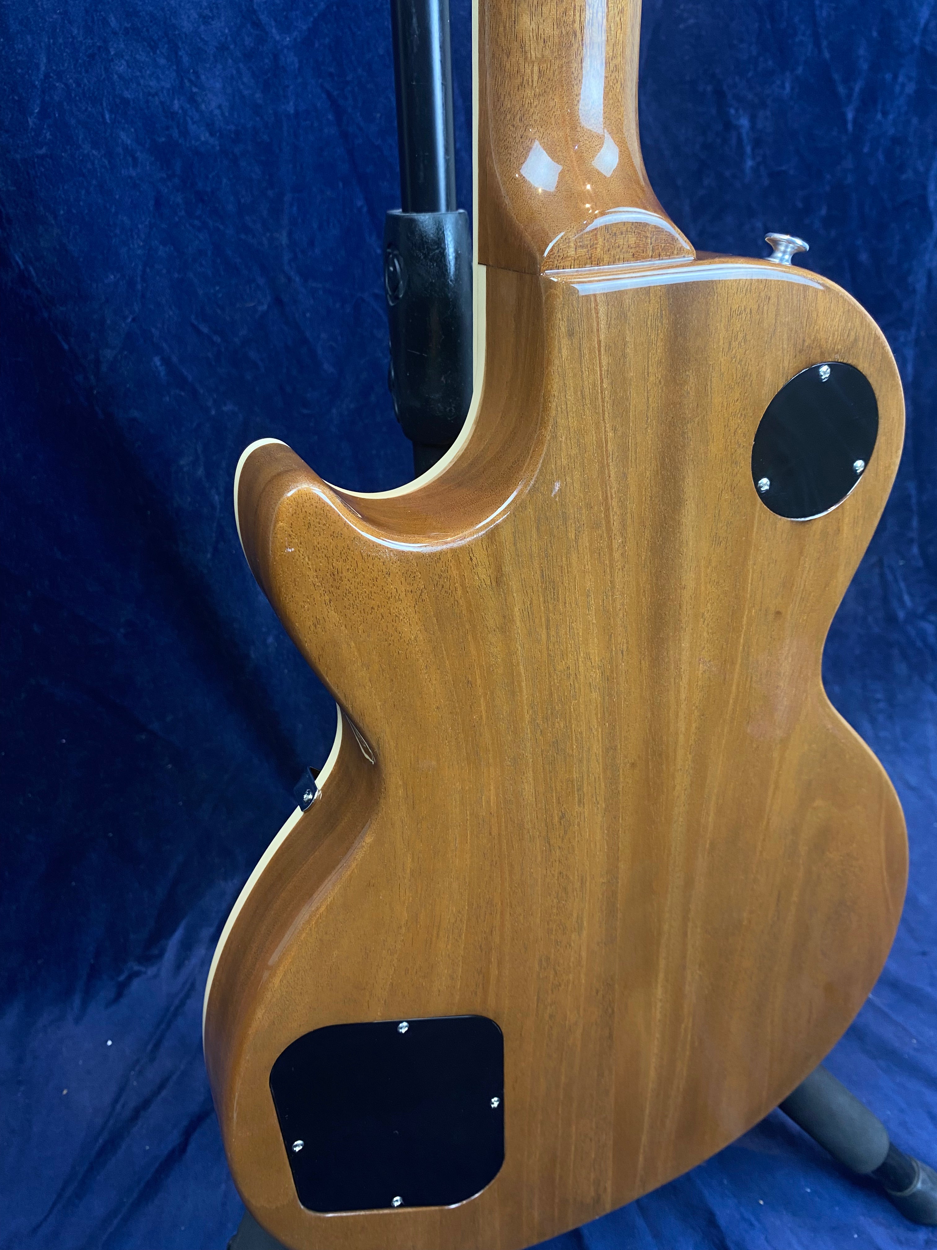 Back view of a brown electric guitar with a glossy finish, showing two black control cavity covers and cream binding along the edge.