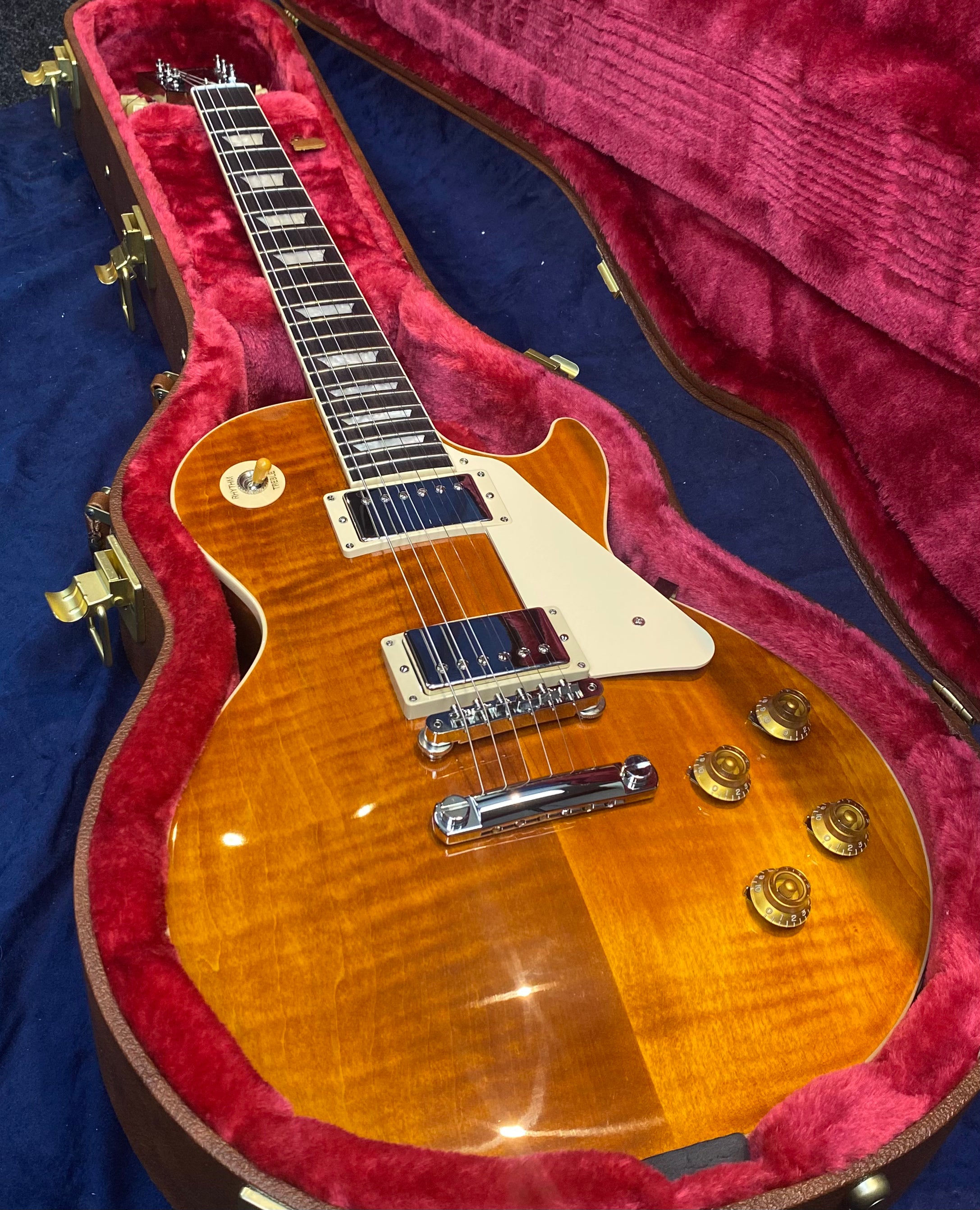 Sunburst electric guitar with chrome hardware, cream pickguard, and amber knobs, resting in a red velvet-lined hard case.
