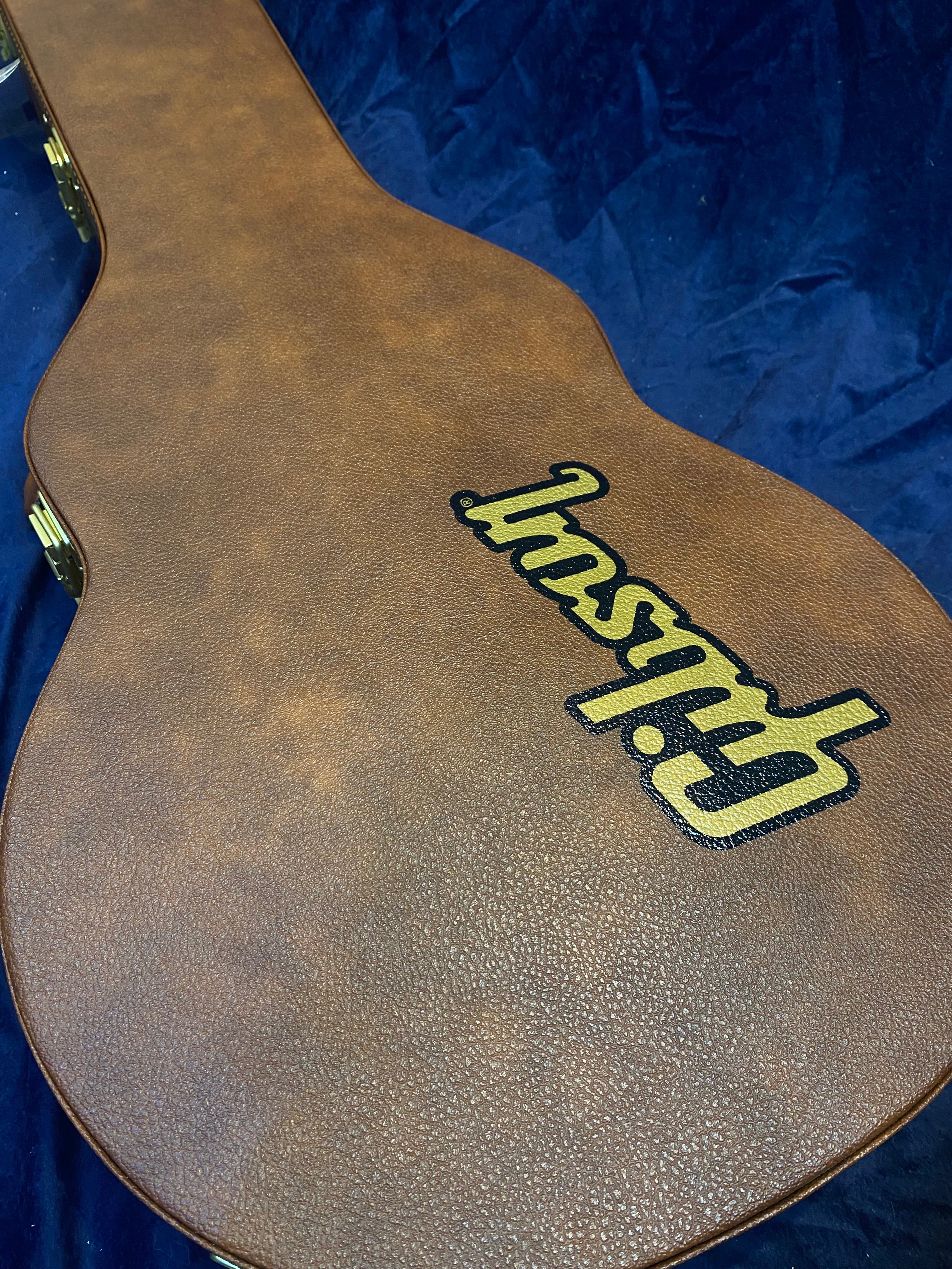 Brown textured hard case for an electric guitar, with the Gibson logo in black and yellow lettering across the top, set against a dark blue background.