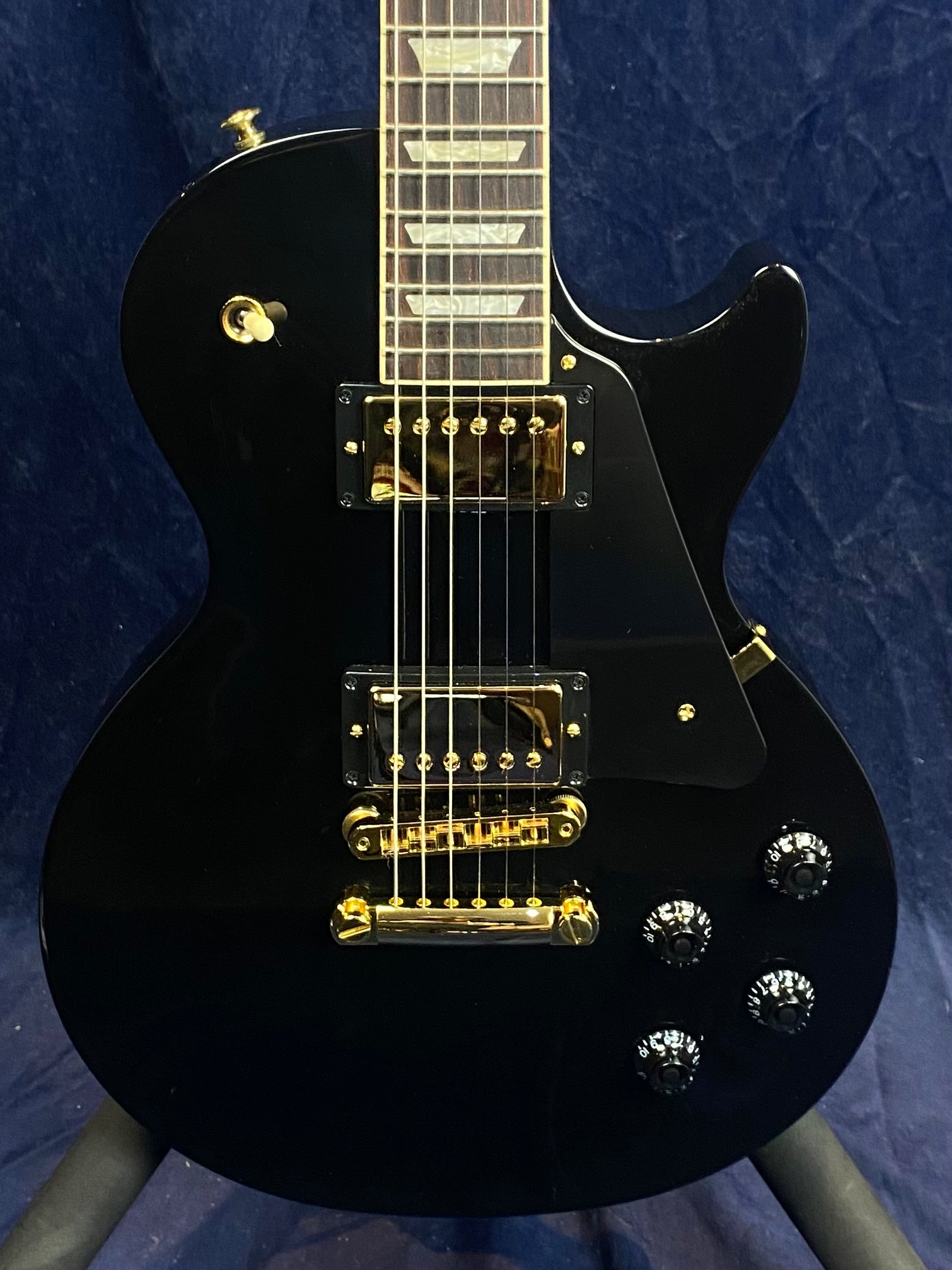 Glossy black electric guitar with gold hardware, two pickups, four black control knobs, and a single cutaway body design.