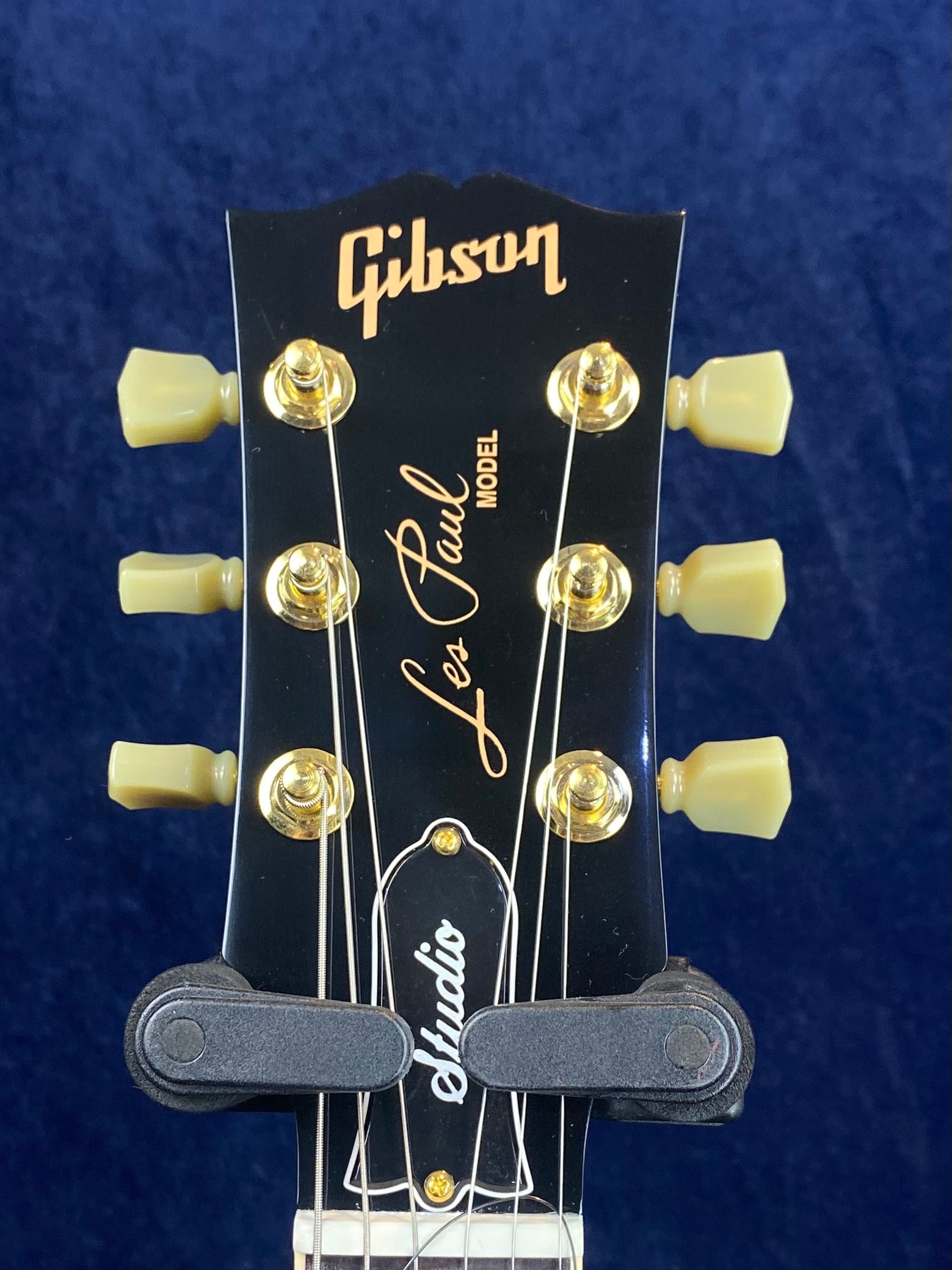 Gibson Les Paul Studio electric guitar headstock with gold tuners, cream pegs, and logo text on a black background.