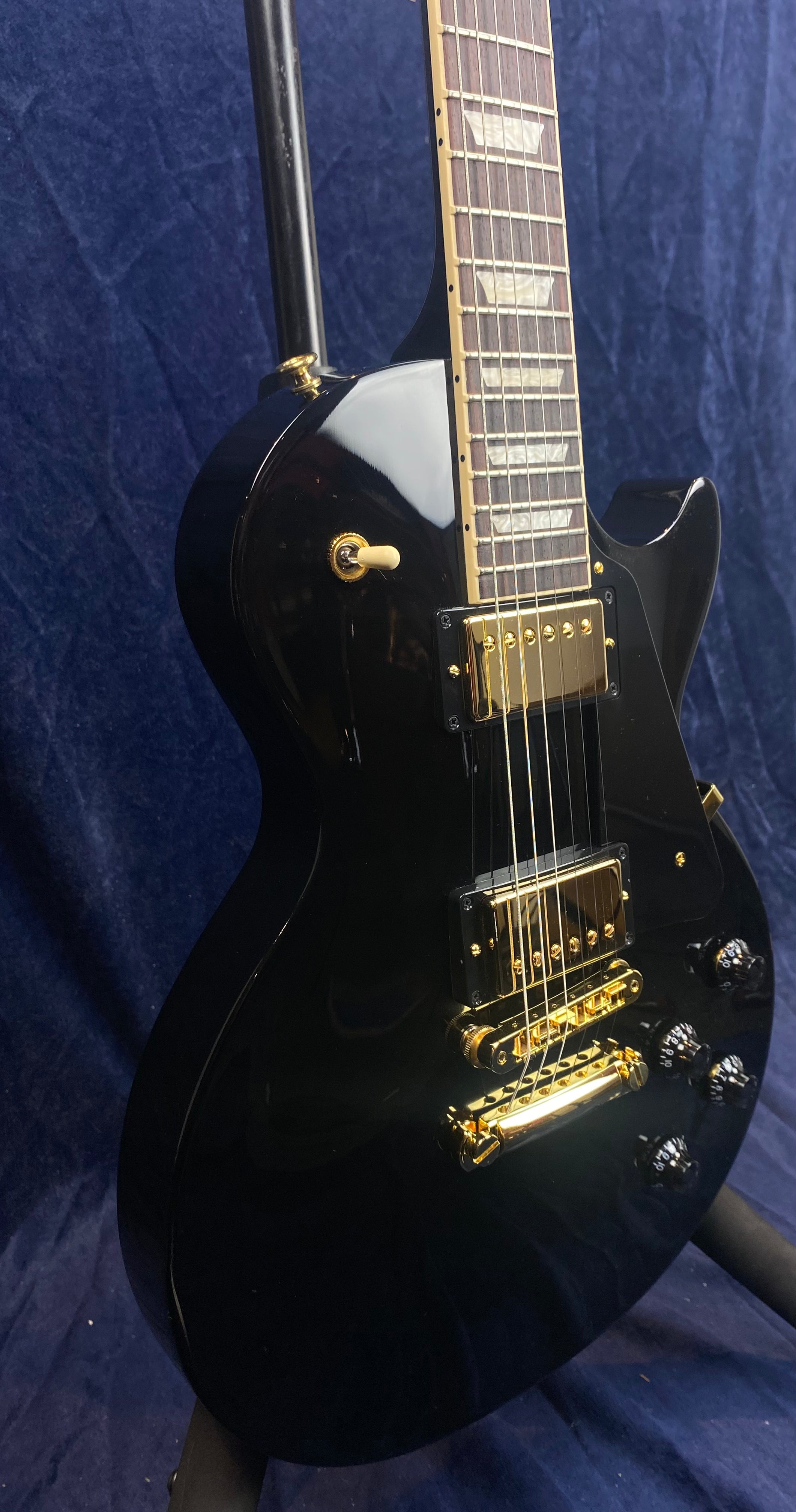 Glossy black electric guitar with gold hardware, two humbucker pickups, four black control knobs, and rectangular pearloid inlays on the fretboard.