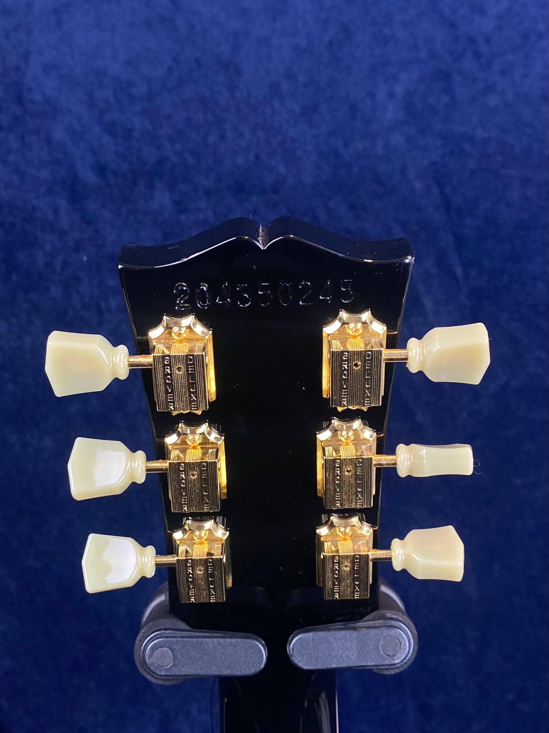 Electric guitar headstock with six gold tuning machines and cream-colored pegs, black finish, and serial number 204350243 engraved at the top.