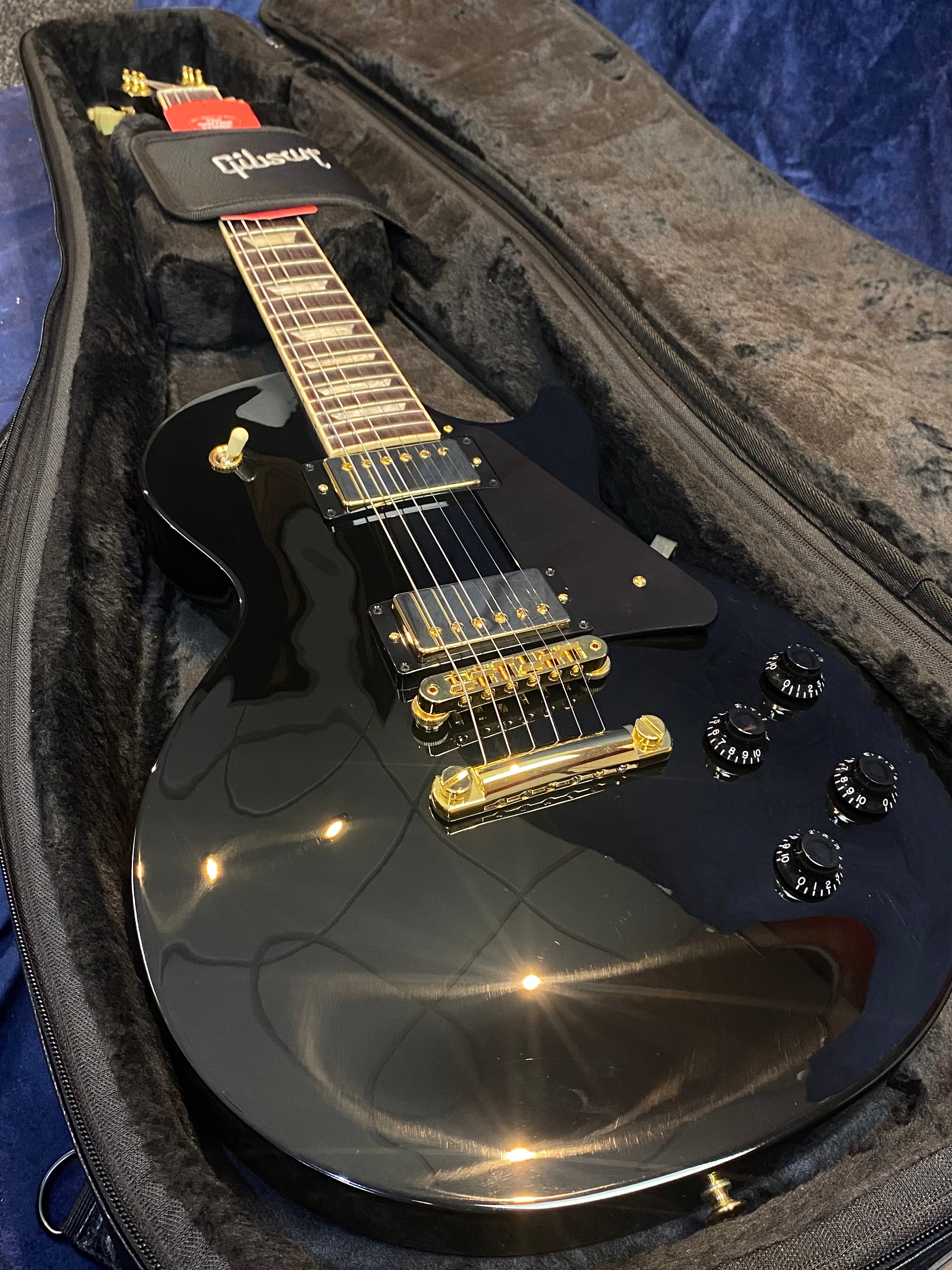 Glossy black electric guitar with gold hardware, black pickguard, and four black control knobs, resting inside a padded Gibson-branded case.