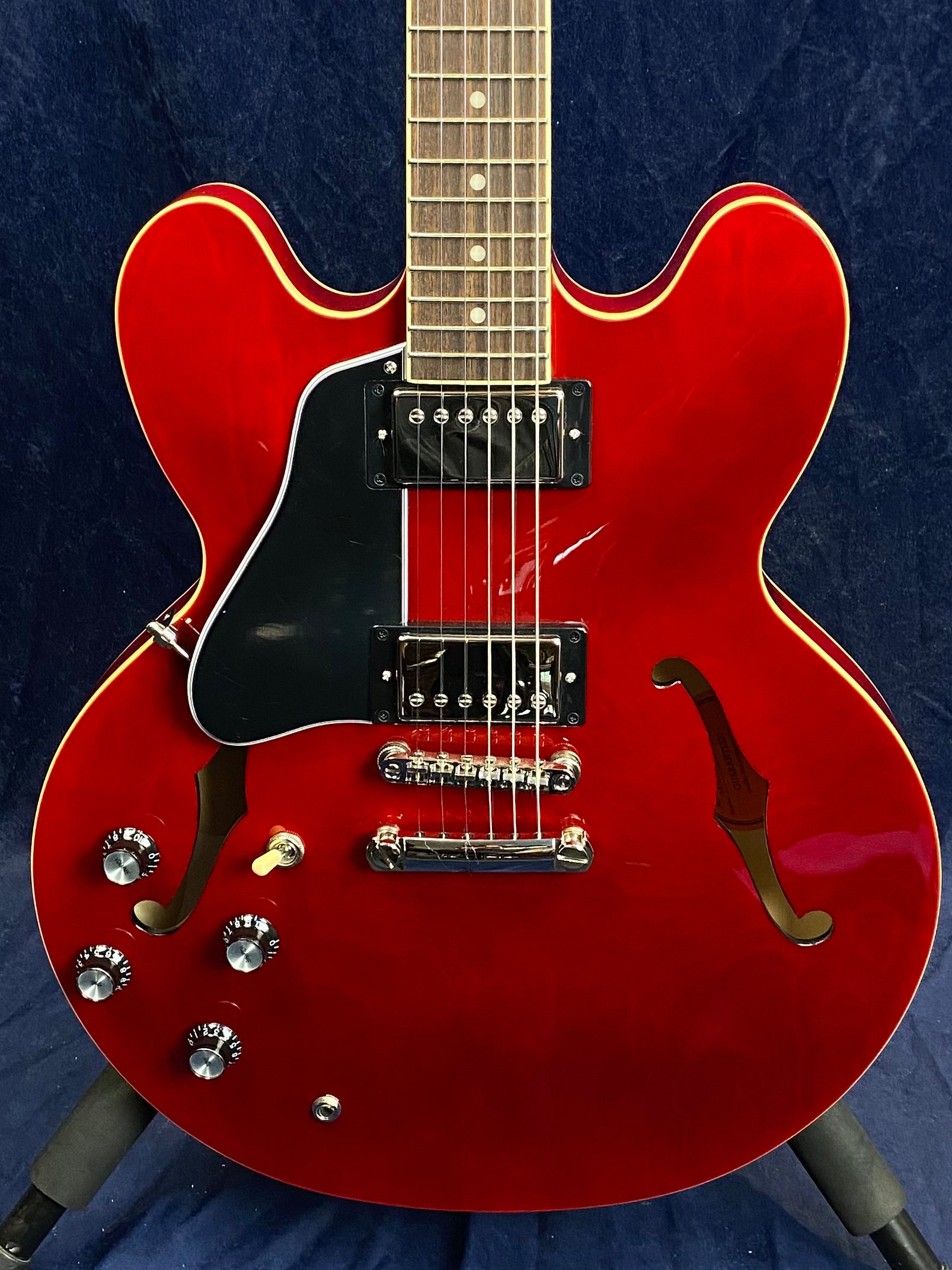 Cherry red semi-hollow electric guitar with two humbucker pickups, black pickguard, four control knobs, and f-shaped sound holes.