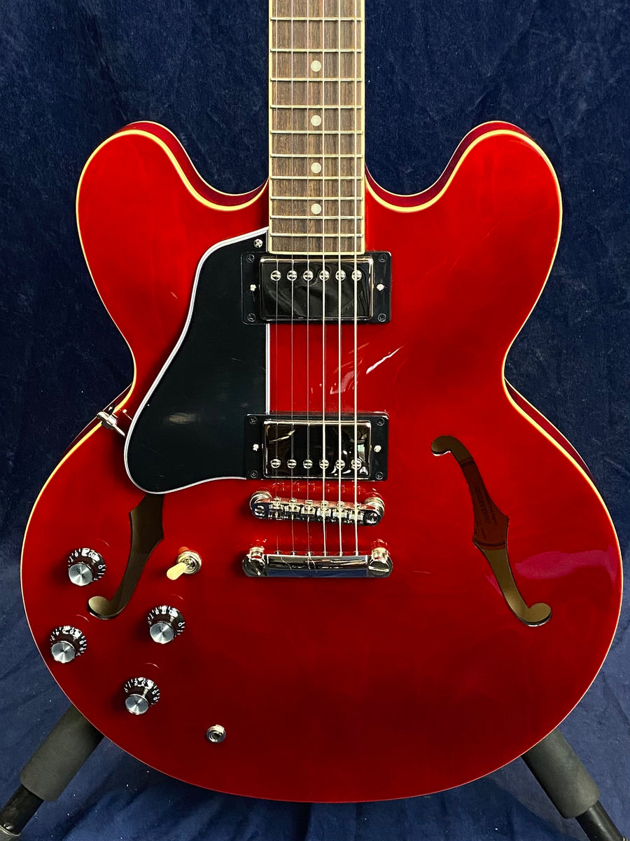 Cherry red semi-hollow electric guitar with two humbucker pickups, black pickguard, four control knobs, and f-shaped sound holes.