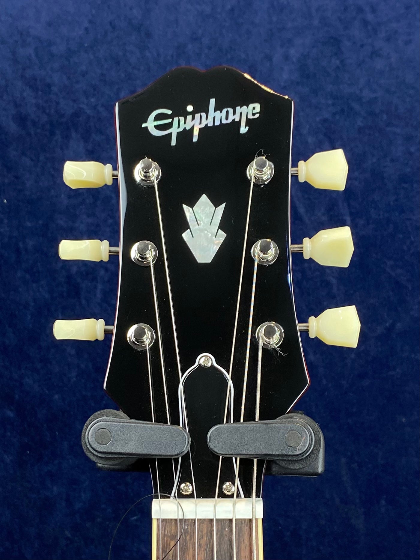 Epiphone electric guitar headstock with six ivory tuning pegs, pearloid logo, and decorative inlay on a dark background.